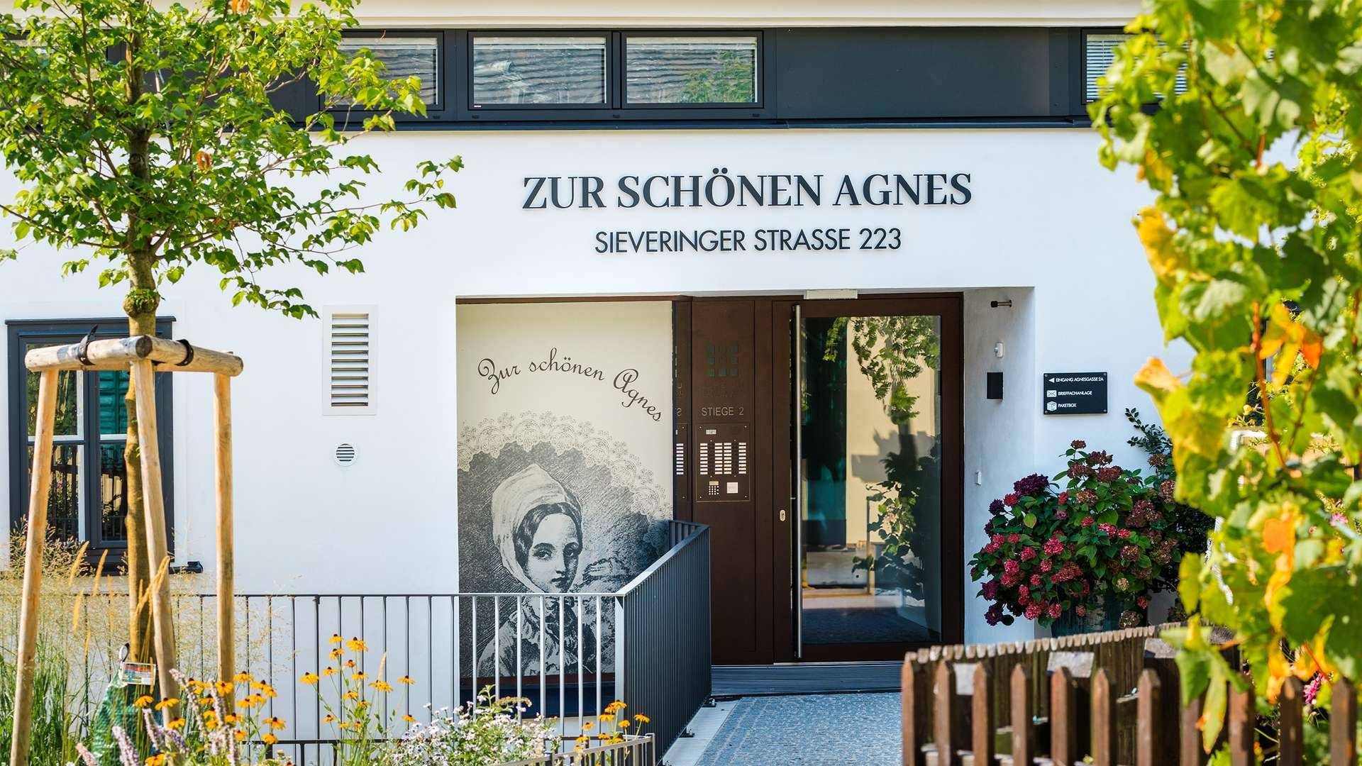 Eingangsbereich des Gebäudes "Zur Schönen Agnes" mit künstlerischer Wandgestaltung und Pflanzen.