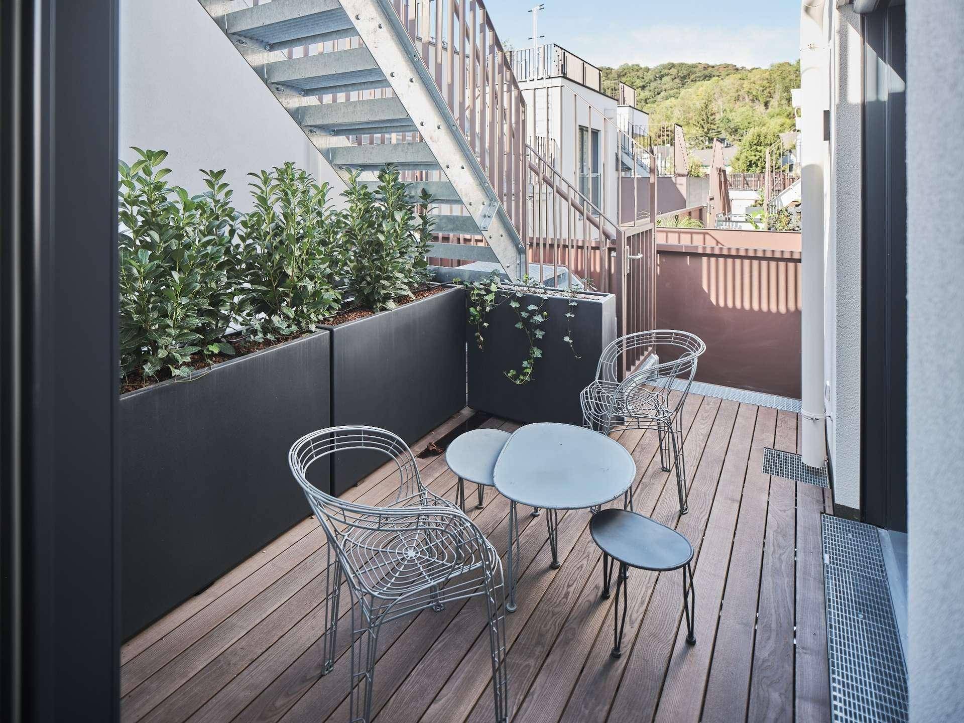 Kleiner Balkon mit Holzboden, modernen Gartenmöbeln und Pflanzen, ideal für entspannte Stunden im Freien.