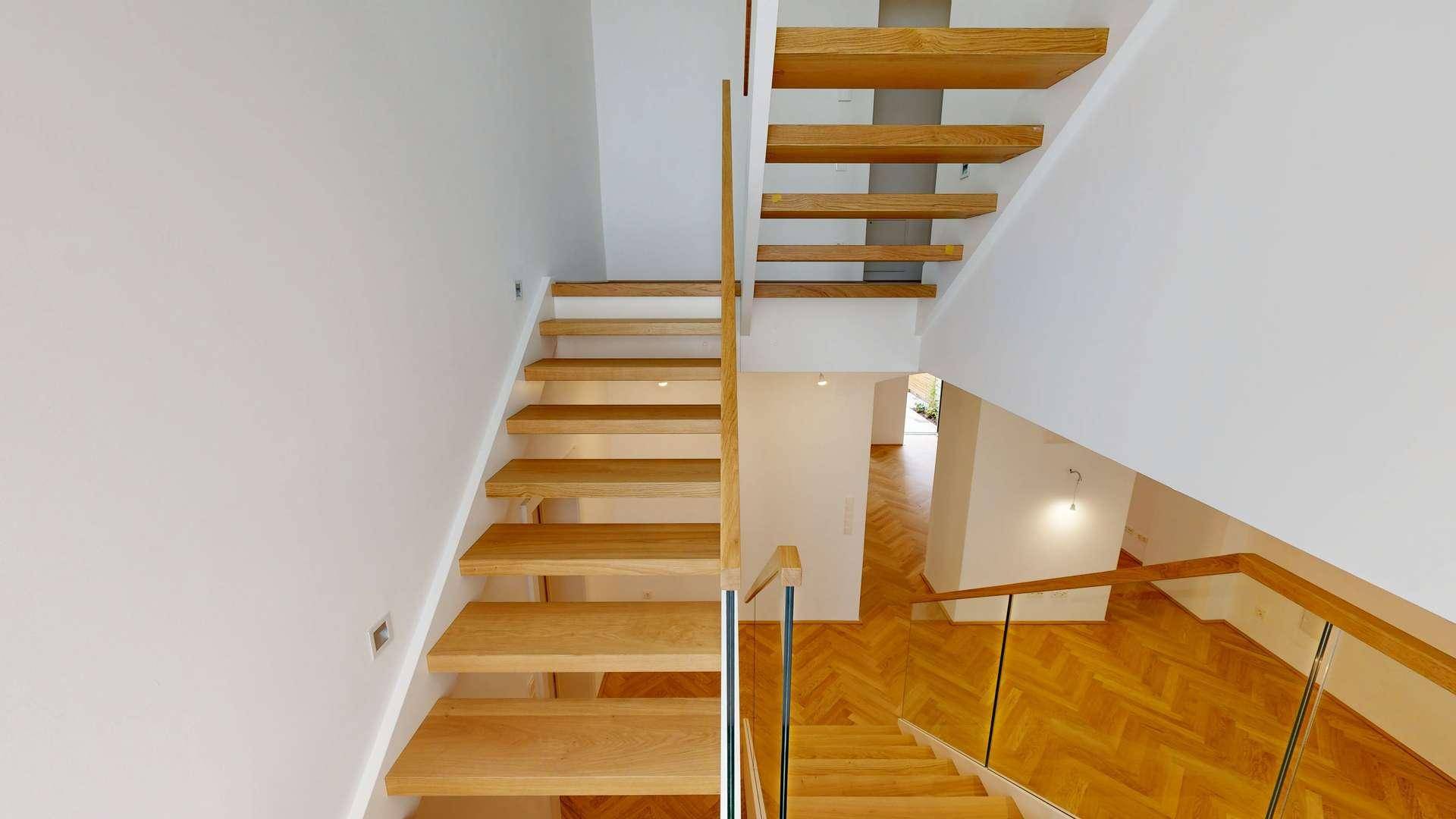 Elegante Holztreppe mit Glasgeländer, die die verschiedenen Ebenen des Hauses verbindet.