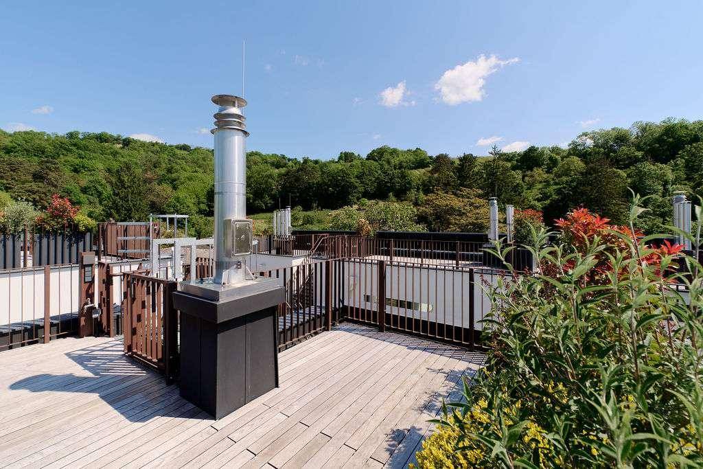 Weitläufige Dachterrasse mit Holzbelag und Geländer, umgeben von grünen Hügeln und Natur.