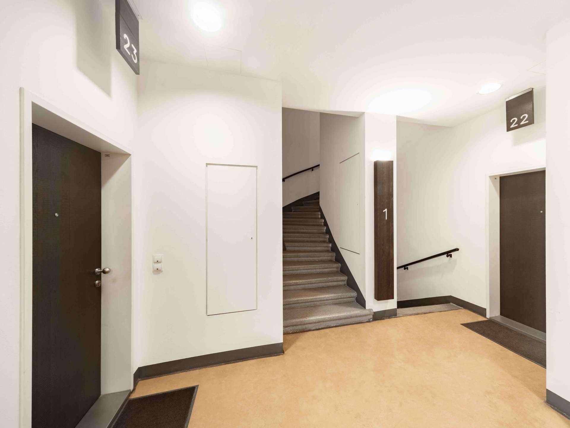 Heller Hausflur mit Treppenaufgang, modernen Türen und minimalistischem Design.