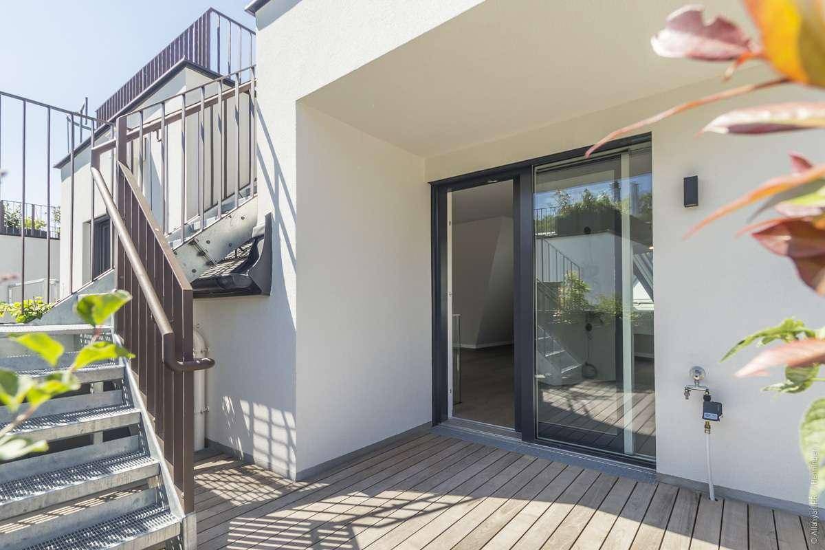 Sonniger Terrassenbereich mit Holzbelag und direktem Zugang zu den Innenräumen durch eine Glasschiebetür.