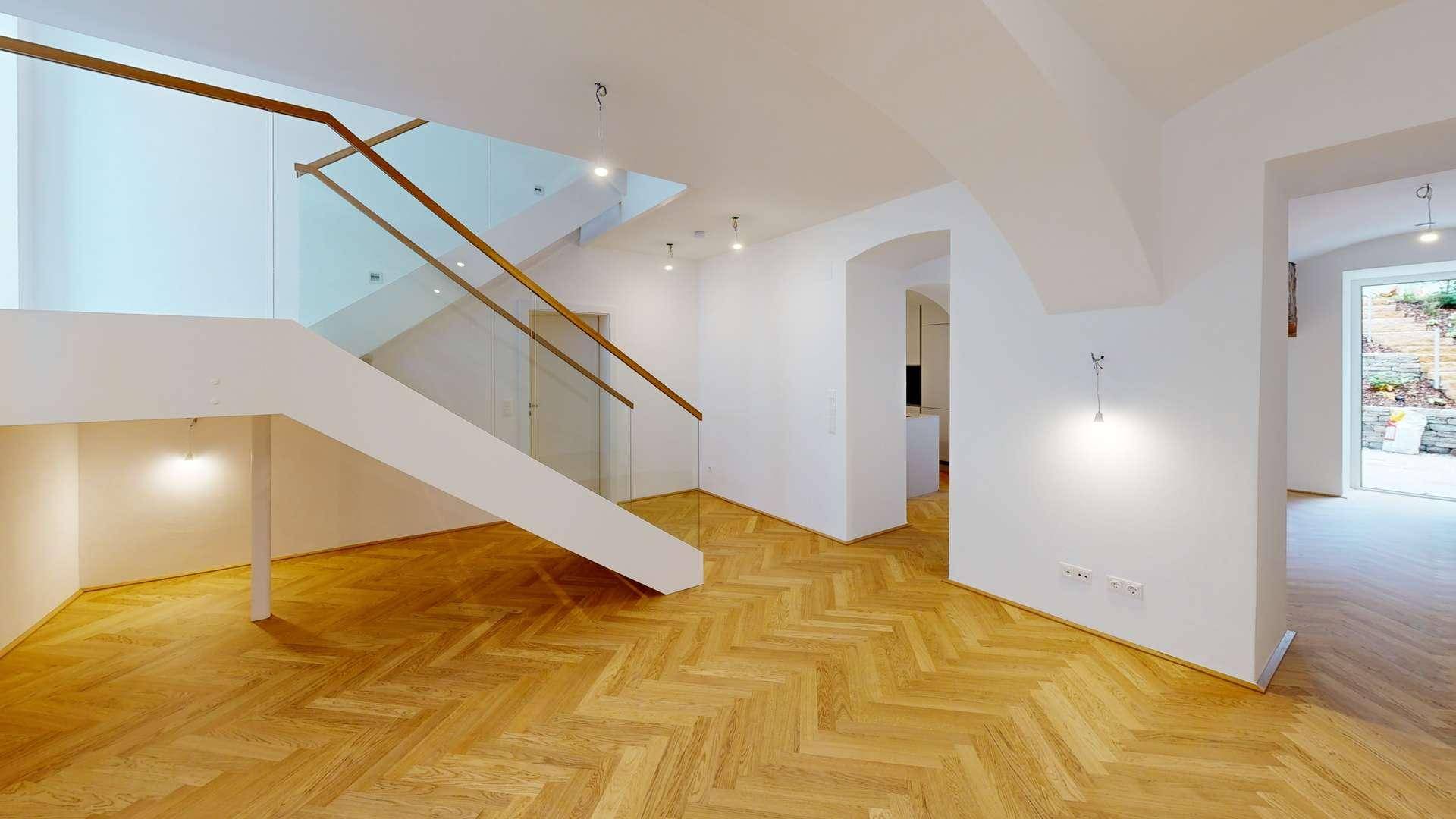 Geräumiger, heller Wohnbereich mit eleganter Holztreppe, Glasgeländer und Zugang zum Außenbereich.