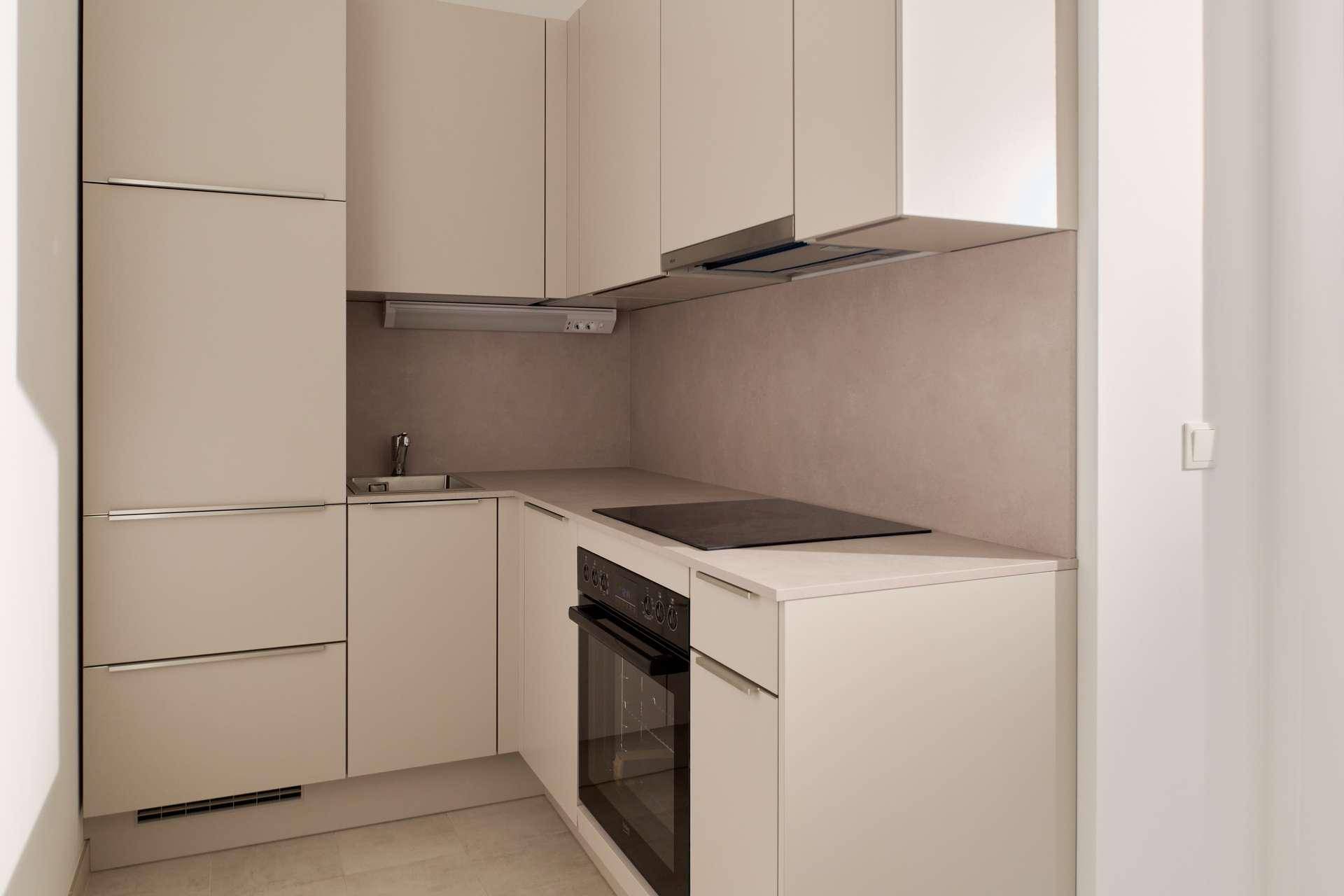 Moderne, kompakte Küchenzeile in hellem Beige mit integrierten Geräten und Kochfeld.