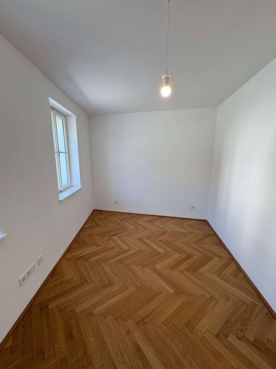 Leerer Raum mit elegantem Fischgrätparkett und einem Fenster, ideal für ein Schlafzimmer.