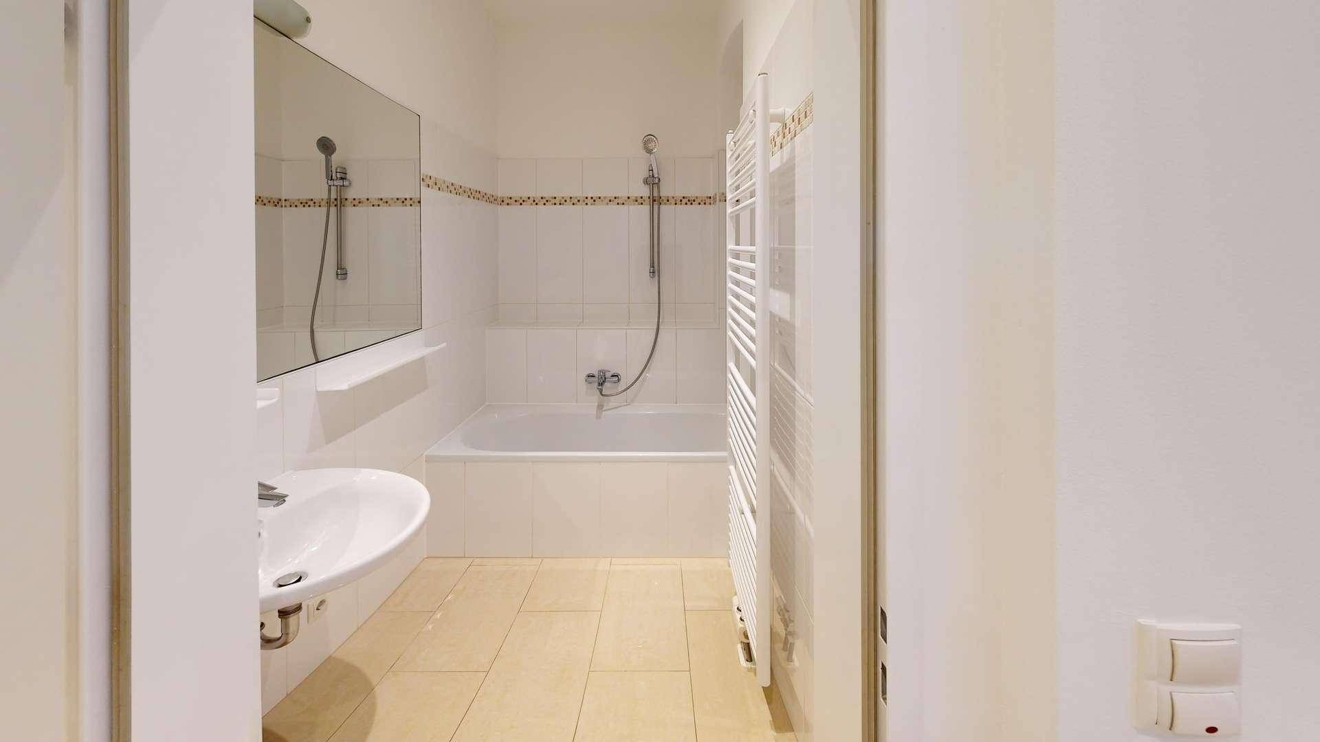 Funktionales Badezimmer mit Badewanne, Waschbecken und beheiztem Handtuchhalter.