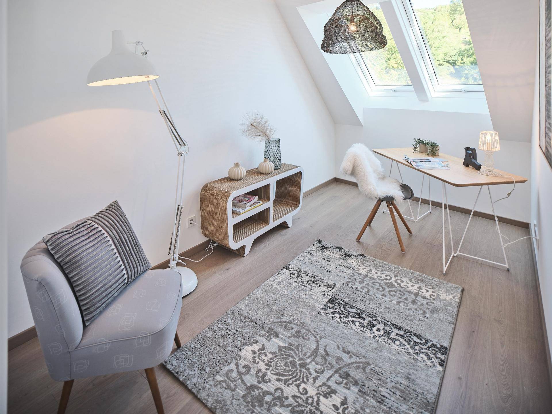 Heller Arbeitsbereich im Dachgeschoss mit Schreibtisch, modernem Sessel und schrägen Dachfenstern.