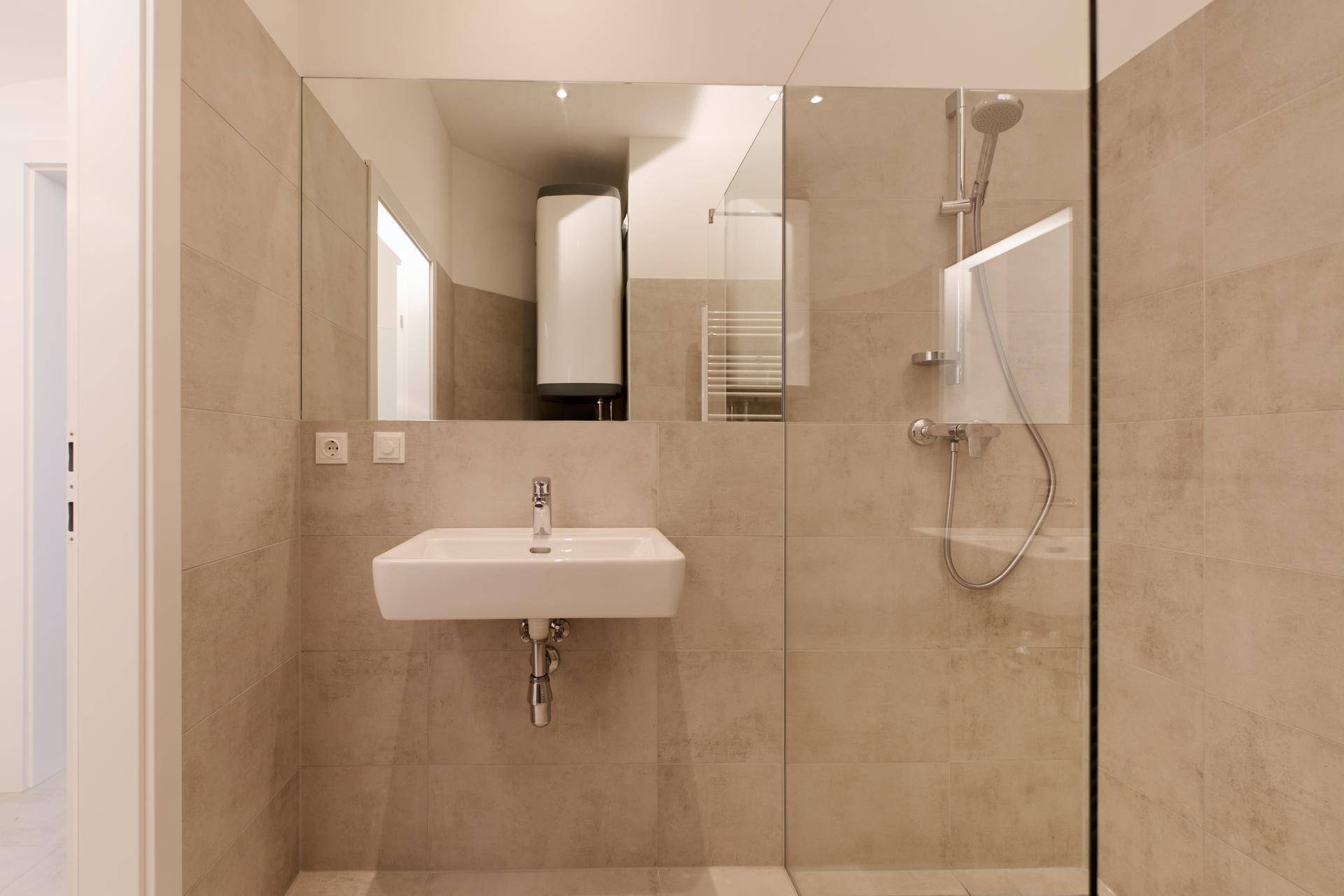 Modernes Badezimmer mit wandhängendem Waschbecken, großer Spiegelfläche und begehbarer Dusche.