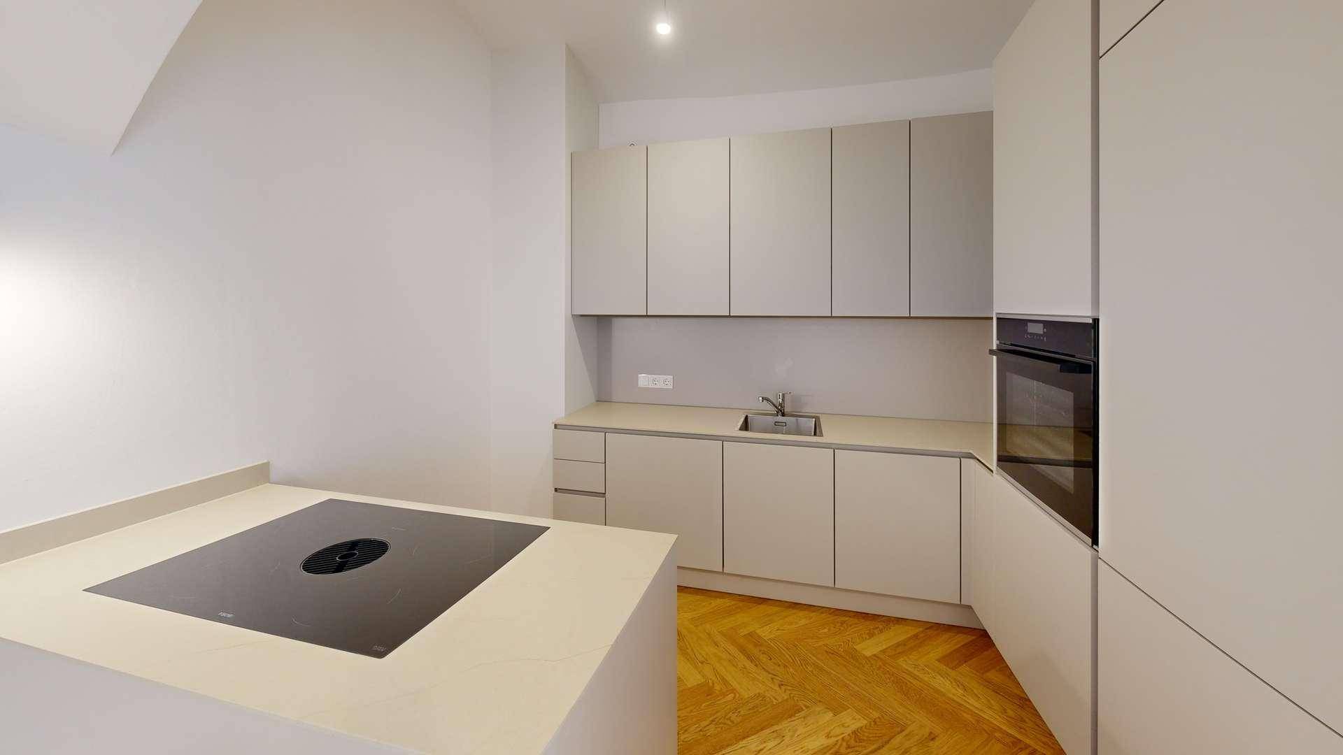 Moderne Küche mit hellgrauen Schränken, Induktionskochfeld auf der Insel und integriertem Backofen.