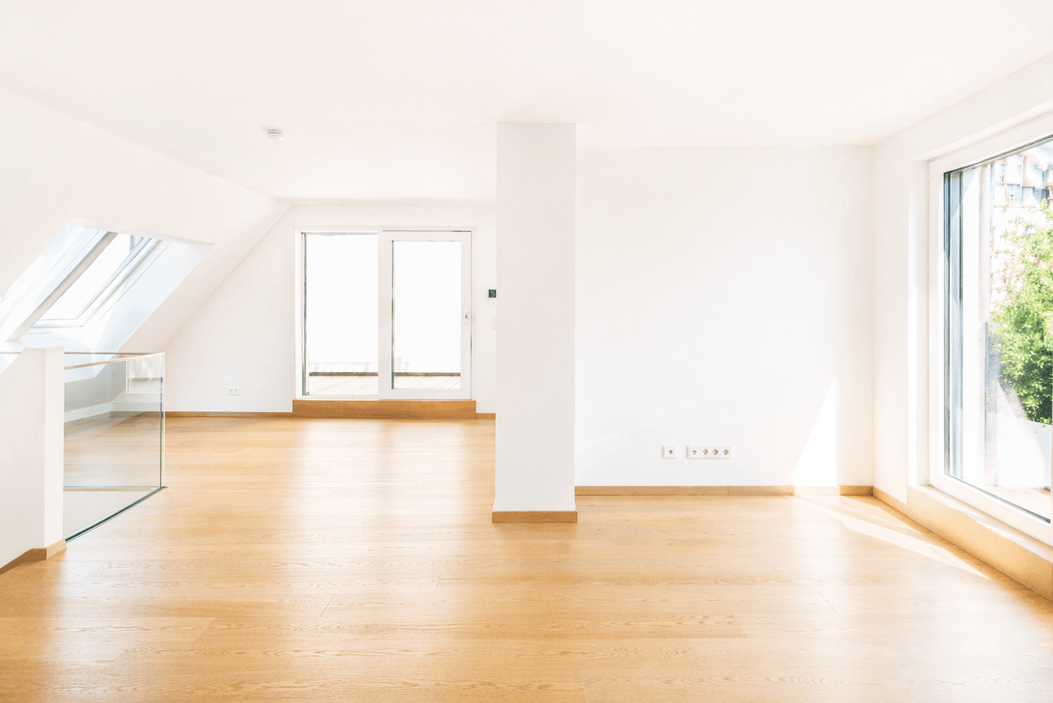 Helles, offenes Wohnzimmer mit Holzboden, Dachfenstern und Zugang zu einem Außenbereich.