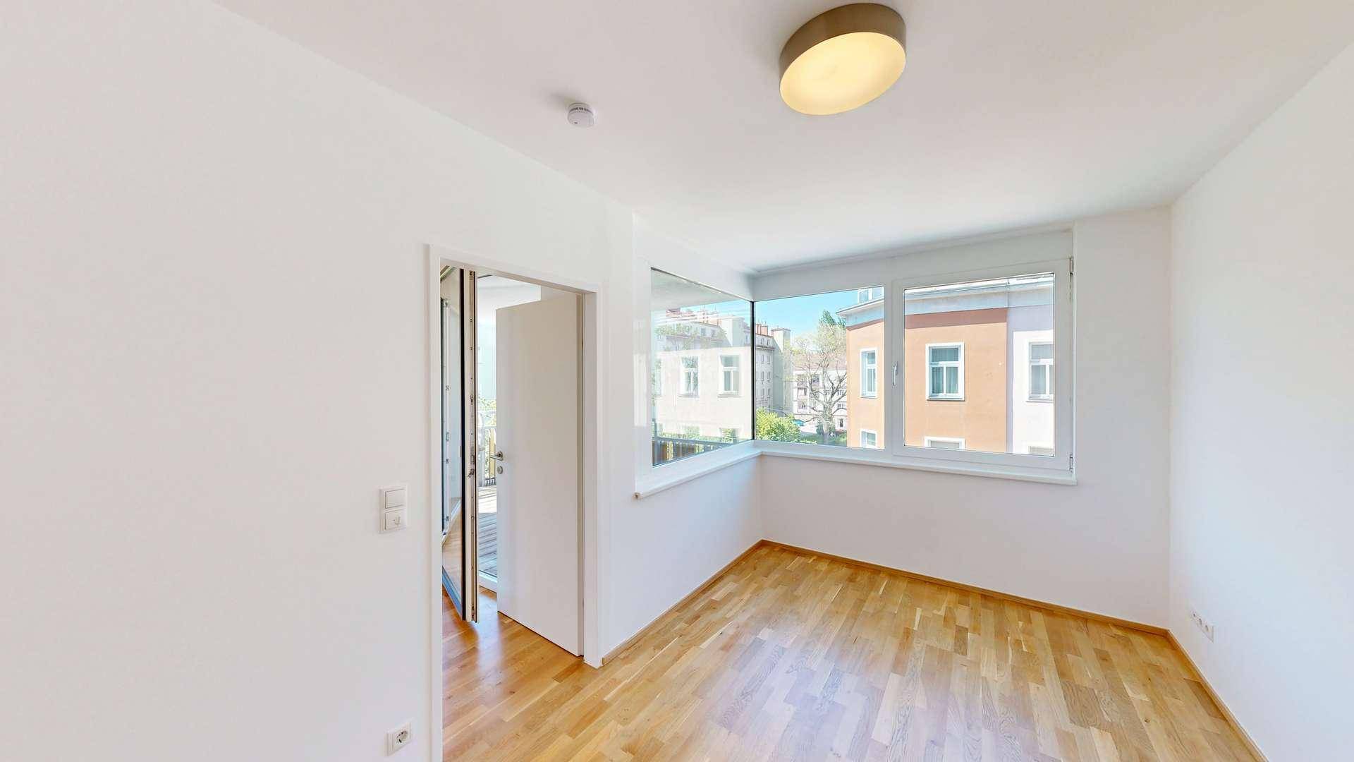 Helles Schlafzimmer mit Parkettboden und Zugang zu einem Balkon, bietet viel Tageslicht.