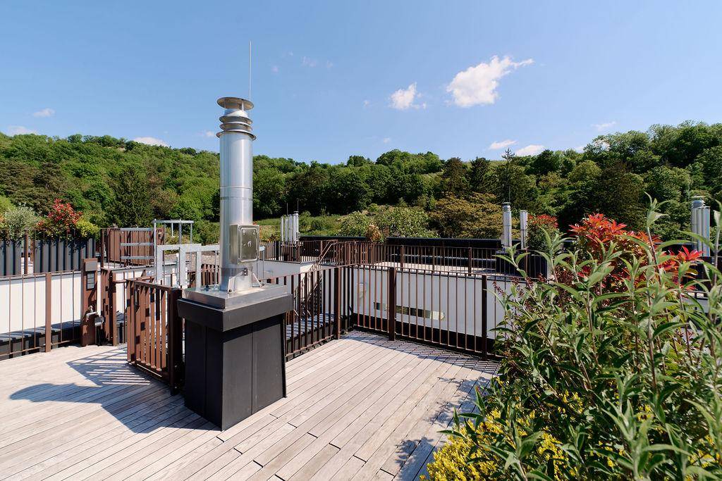 Weitläufige Dachterrasse mit Holzboden, Bepflanzung und Panoramablick auf die umliegende Hügellandschaft.