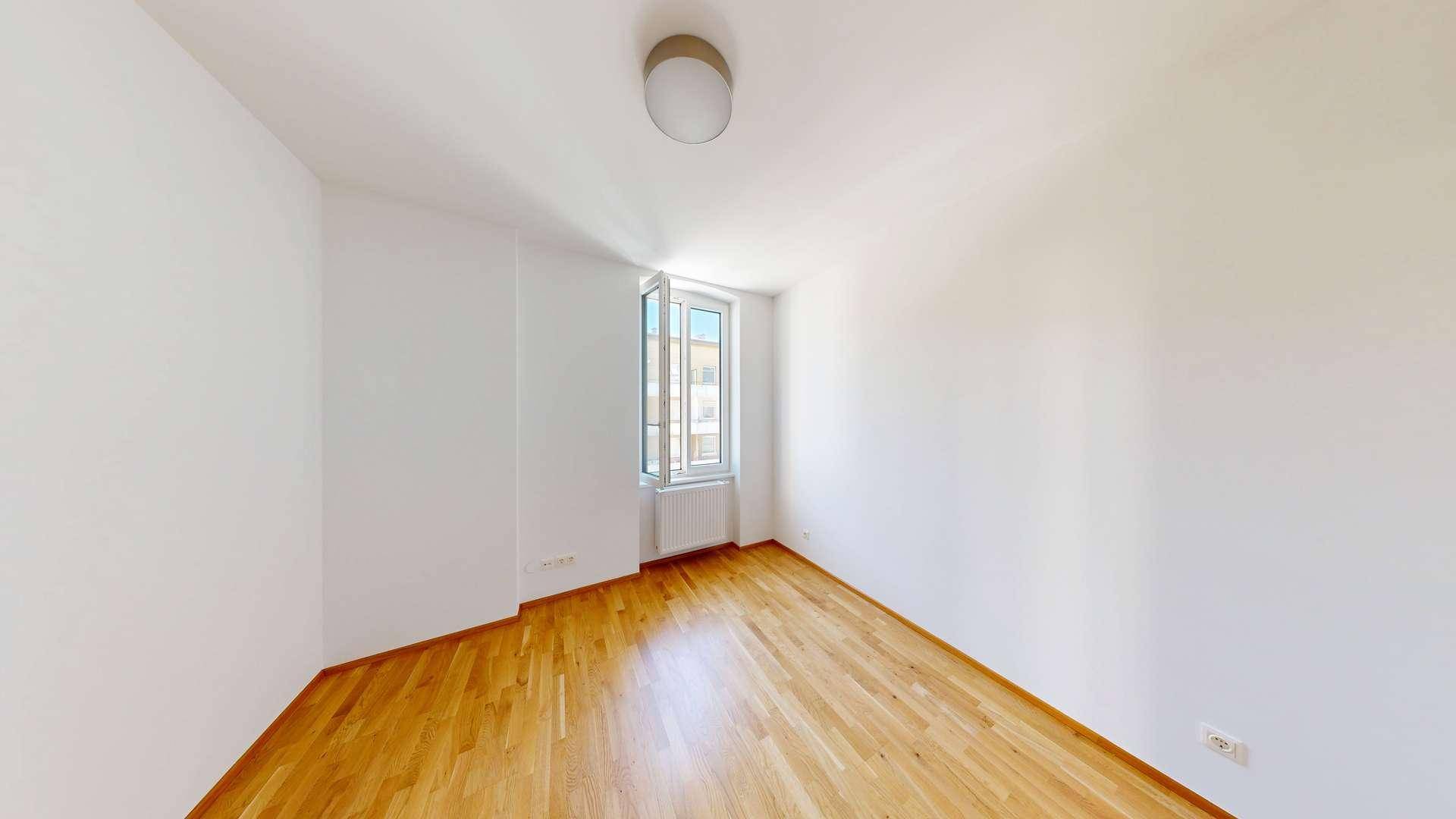 Ruhiges Schlafzimmer mit hellem Parkettboden und einem großen Fenster für viel Tageslicht.