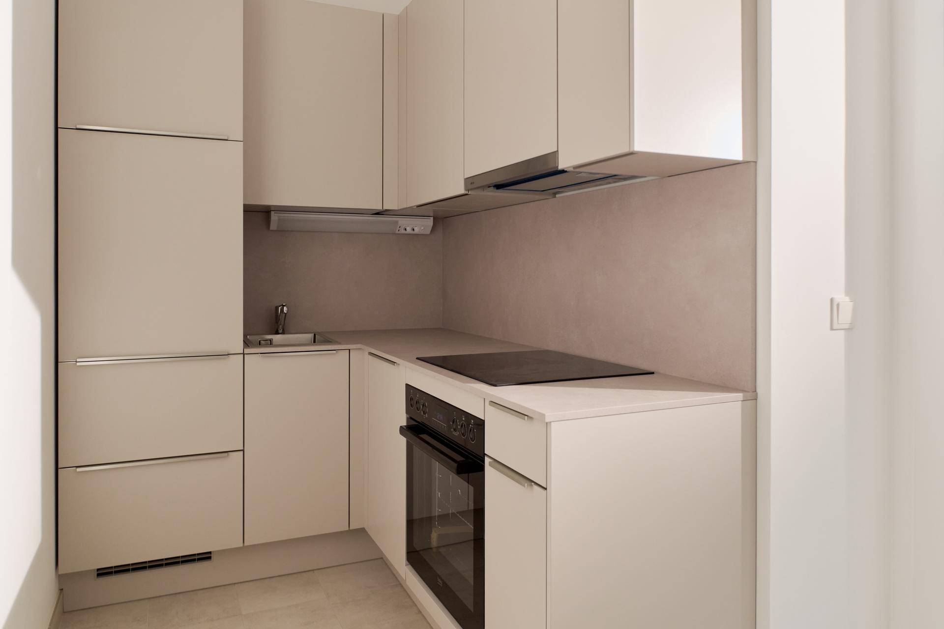 Moderne Küchenzeile mit beigen Schränken, integriertem Backofen und Induktionskochfeld.