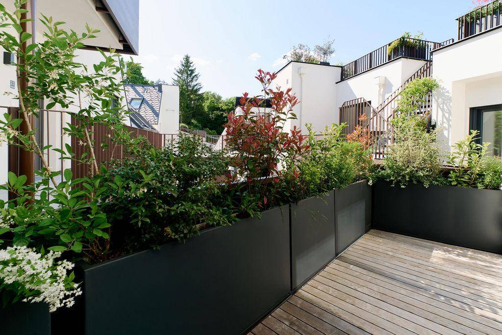 Geräumige Holzterrasse mit großen Pflanzkübeln und üppiger Bepflanzung in einer ruhigen Umgebung.
