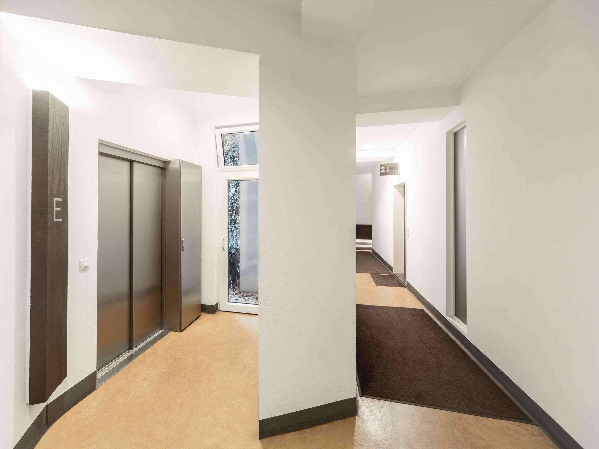 Moderner Hausflur mit Aufzug, Fenster und Zugang zu weiteren Wohnungen.