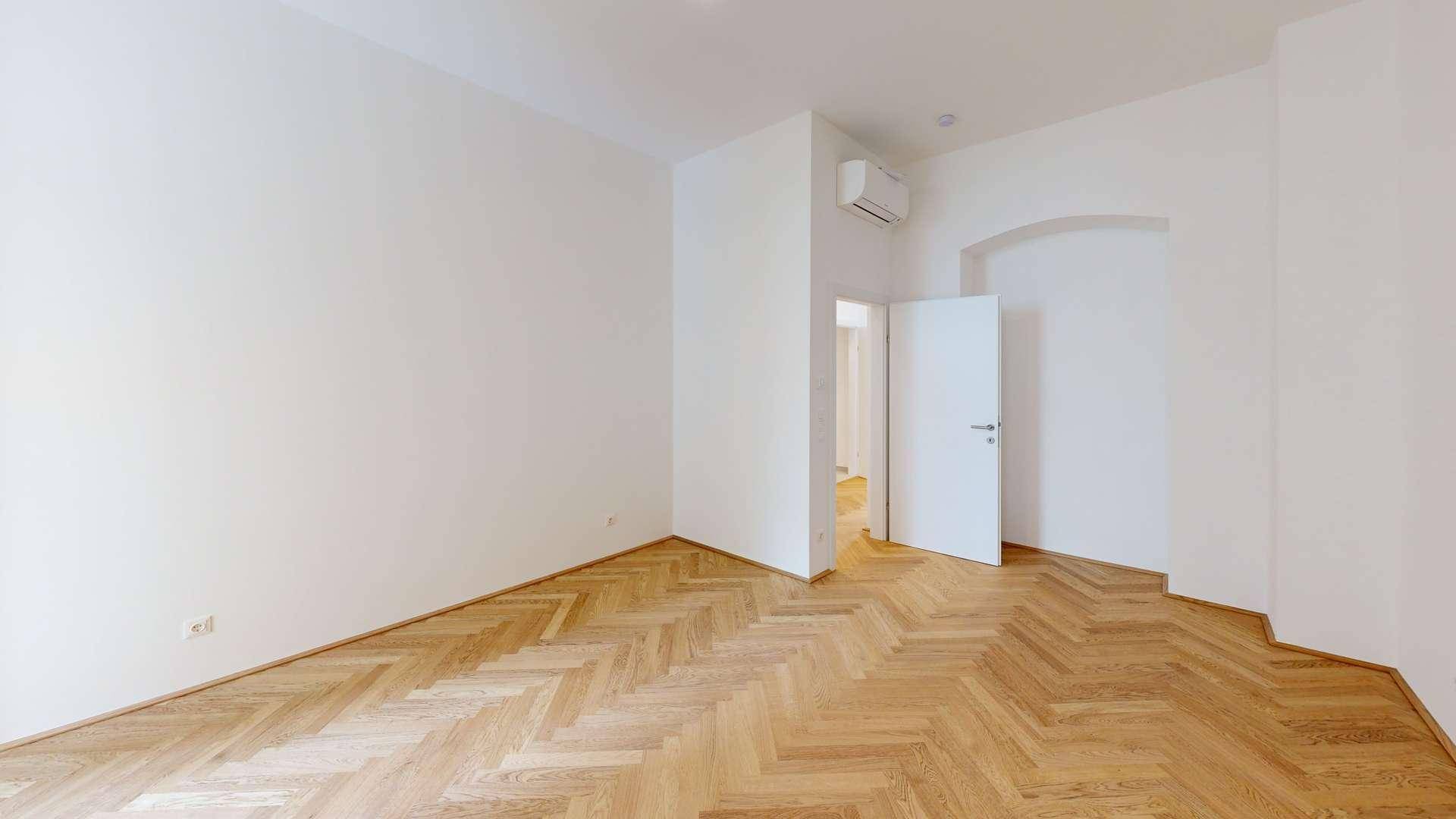 Leeres Zimmer mit Fischgrätparkett, weißen Wänden und Klimaanlage, bereit zur individuellen Gestaltung.