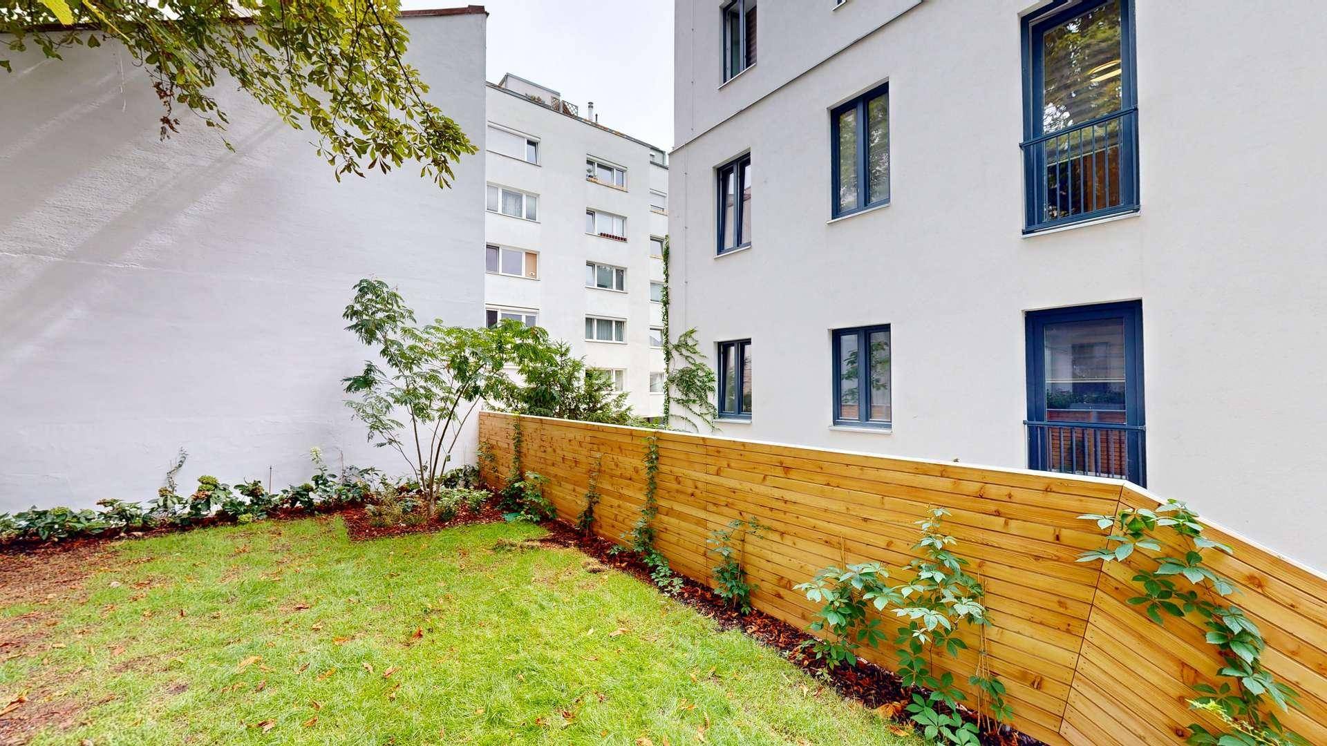 Grüner Gartenbereich mit Rasenfläche, jungen Bäumen und einer modernen Holzumzäunung.