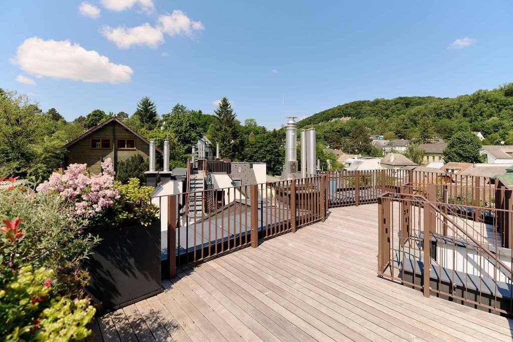 Weitläufige Dachterrasse mit Holzbelag und Panoramablick über die grüne Umgebung.