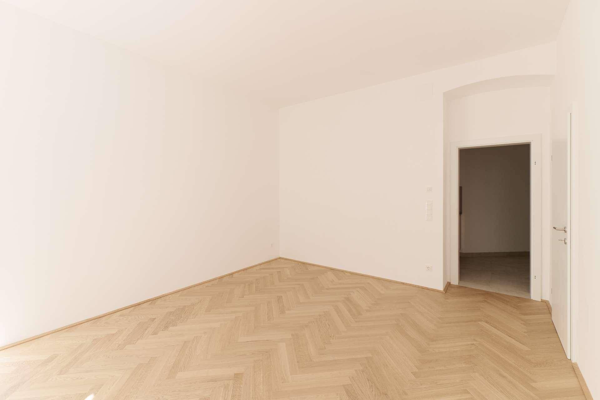 Leeres Zimmer mit Fischgrätparkettboden und weiß gestrichenen Wänden, bereit zur individuellen Gestaltung.