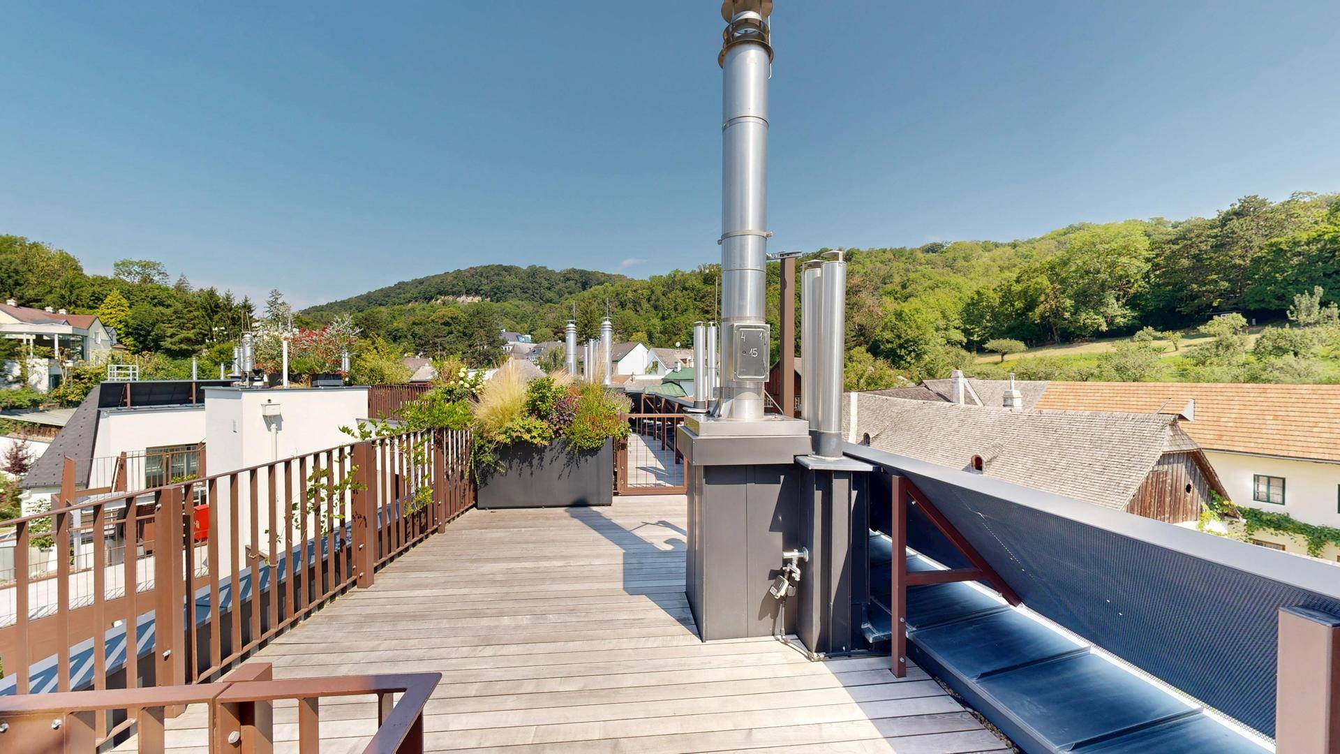 Geräumige Dachterrasse mit Holzdielen, großen Pflanzkübeln und Panoramablick ins Grüne.