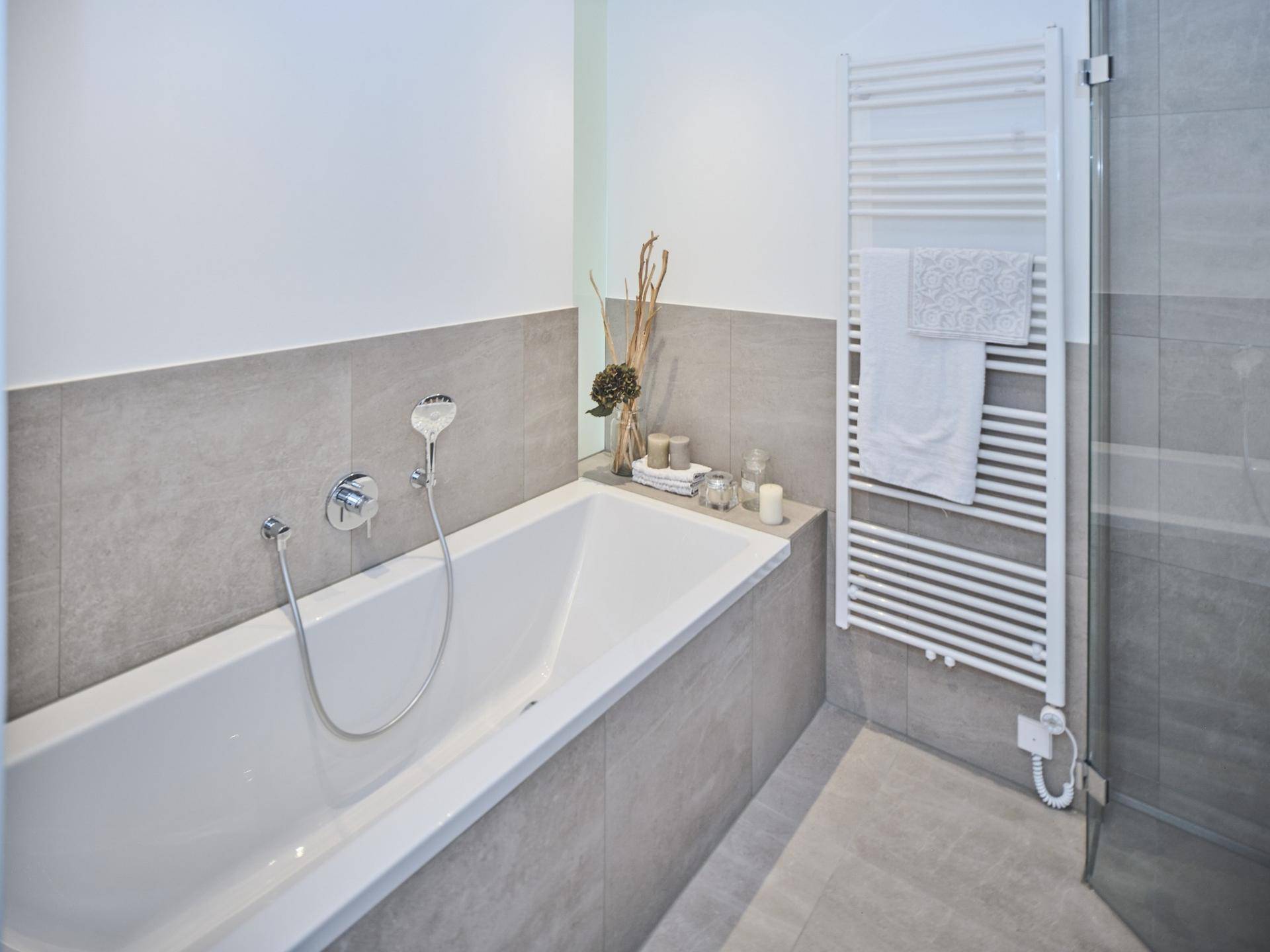 Modernes Badezimmer mit Badewanne, grauen Fliesen und beheiztem Handtuchhalter.