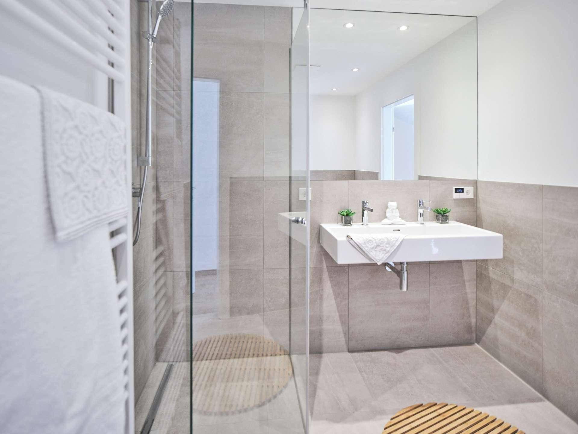 Elegantes Badezimmer mit begehbarer Dusche, modernem Waschbecken und großem Spiegel in Grautönen.
