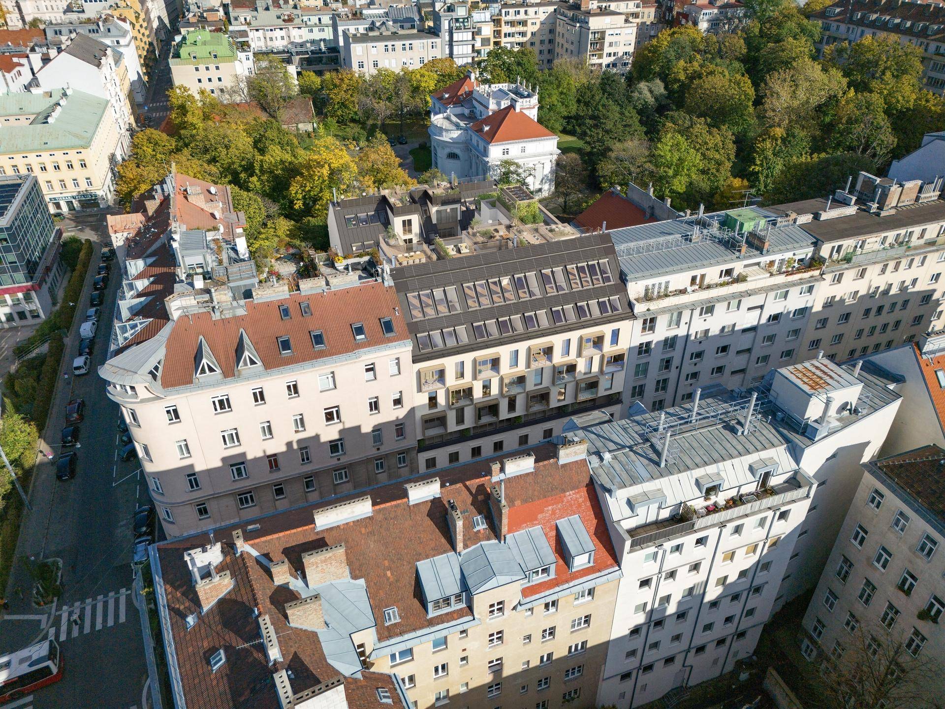Luftaufnahme eines Stadtviertels mit einem modernen Wohngebäude, umgeben von älteren Bauten.