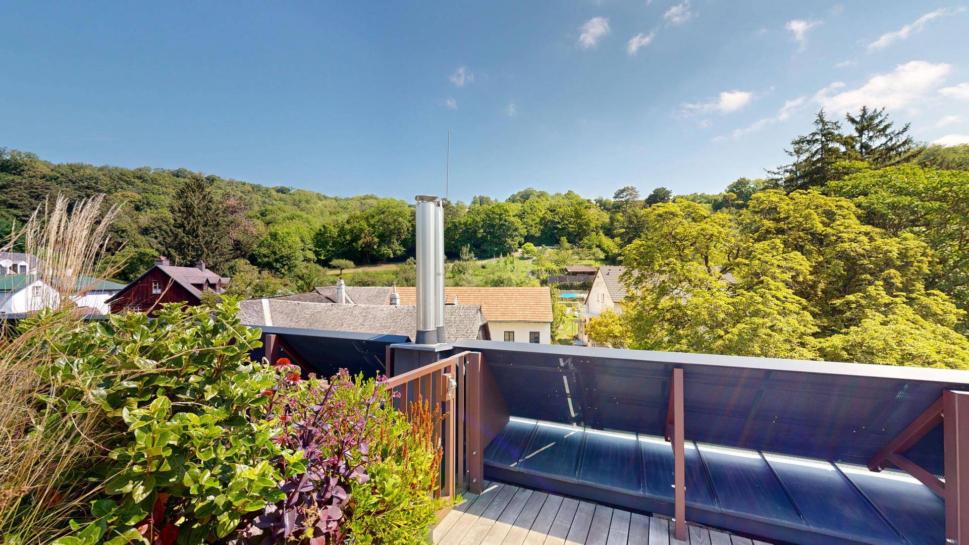 Dachterrasse mit Pflanzen, Holzboden und weitem Blick über die grüne Hügellandschaft.