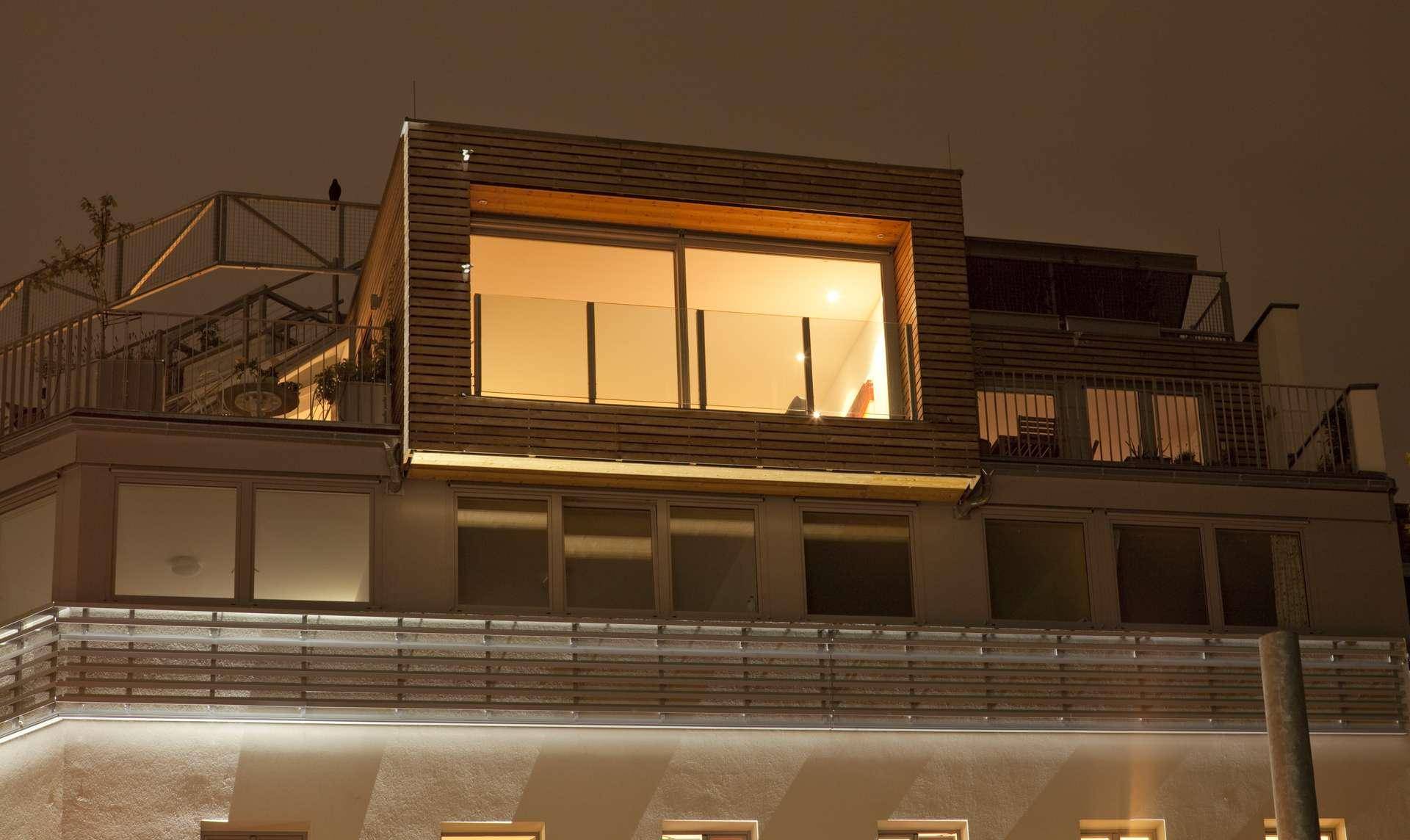 Moderne Dachaufstockung mit großen Fenstern und Holzverkleidung bei Nacht.