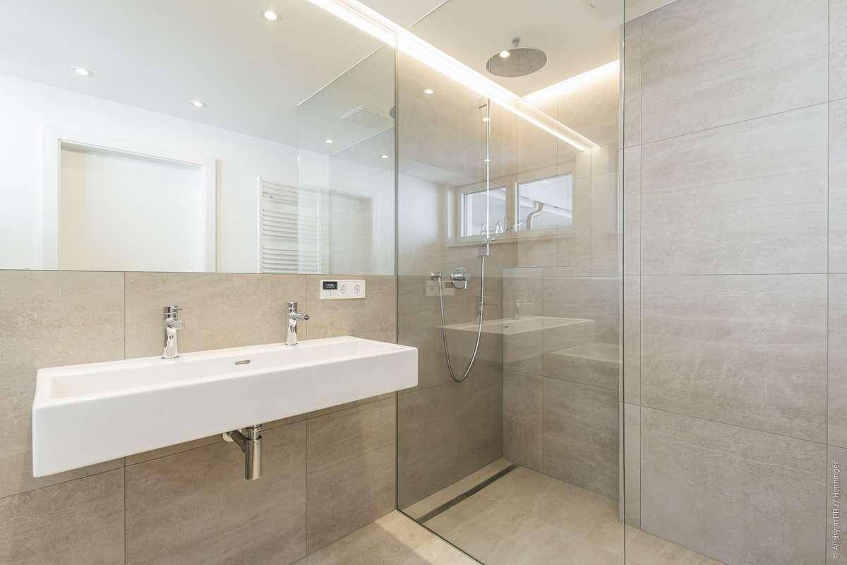 Modernes Badezimmer mit großer begehbarer Dusche, Doppelwaschbecken und hellen Fliesen.