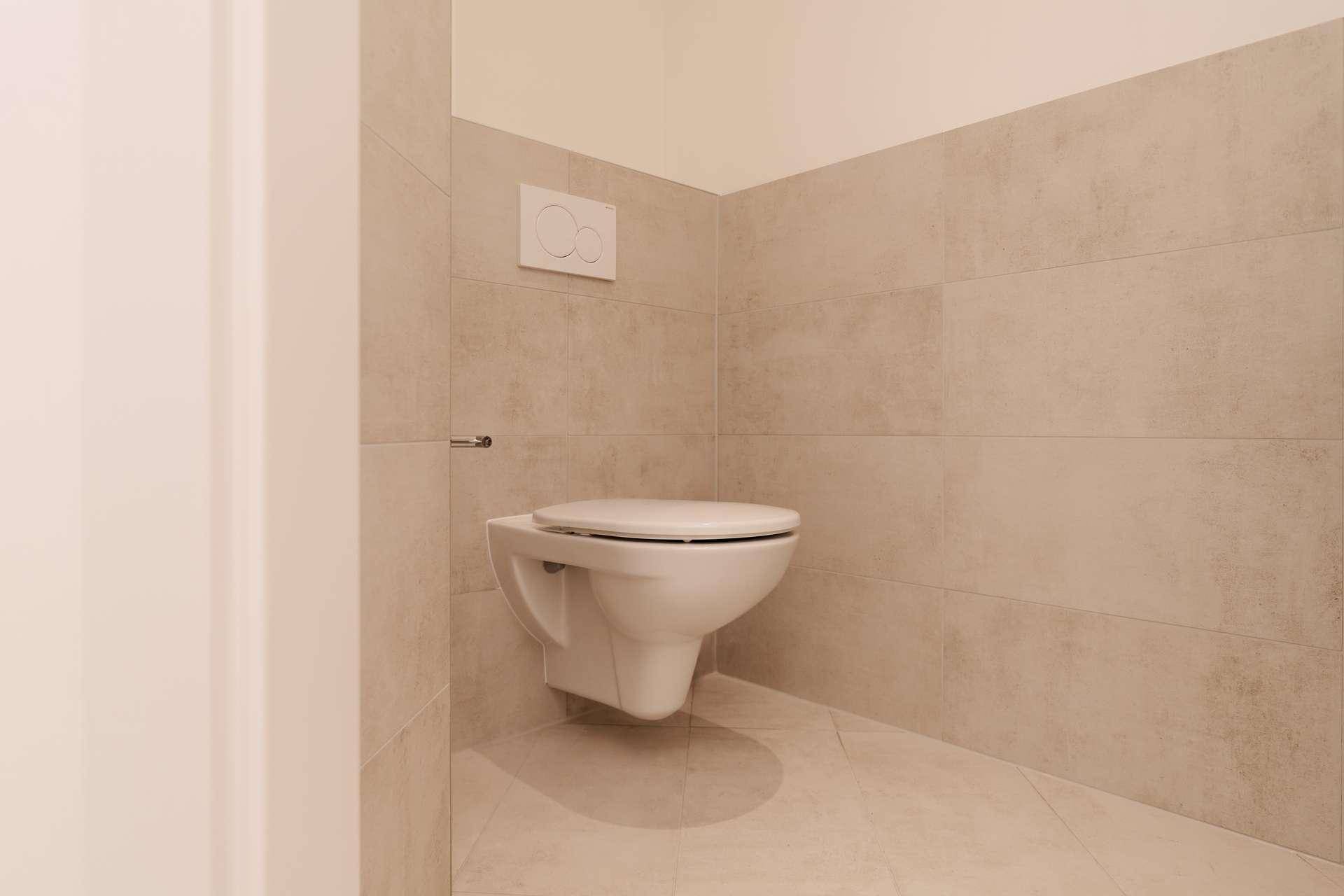Separates WC mit wandhängender Toilette und modernen, hellen Fliesen, funktional und sauber.