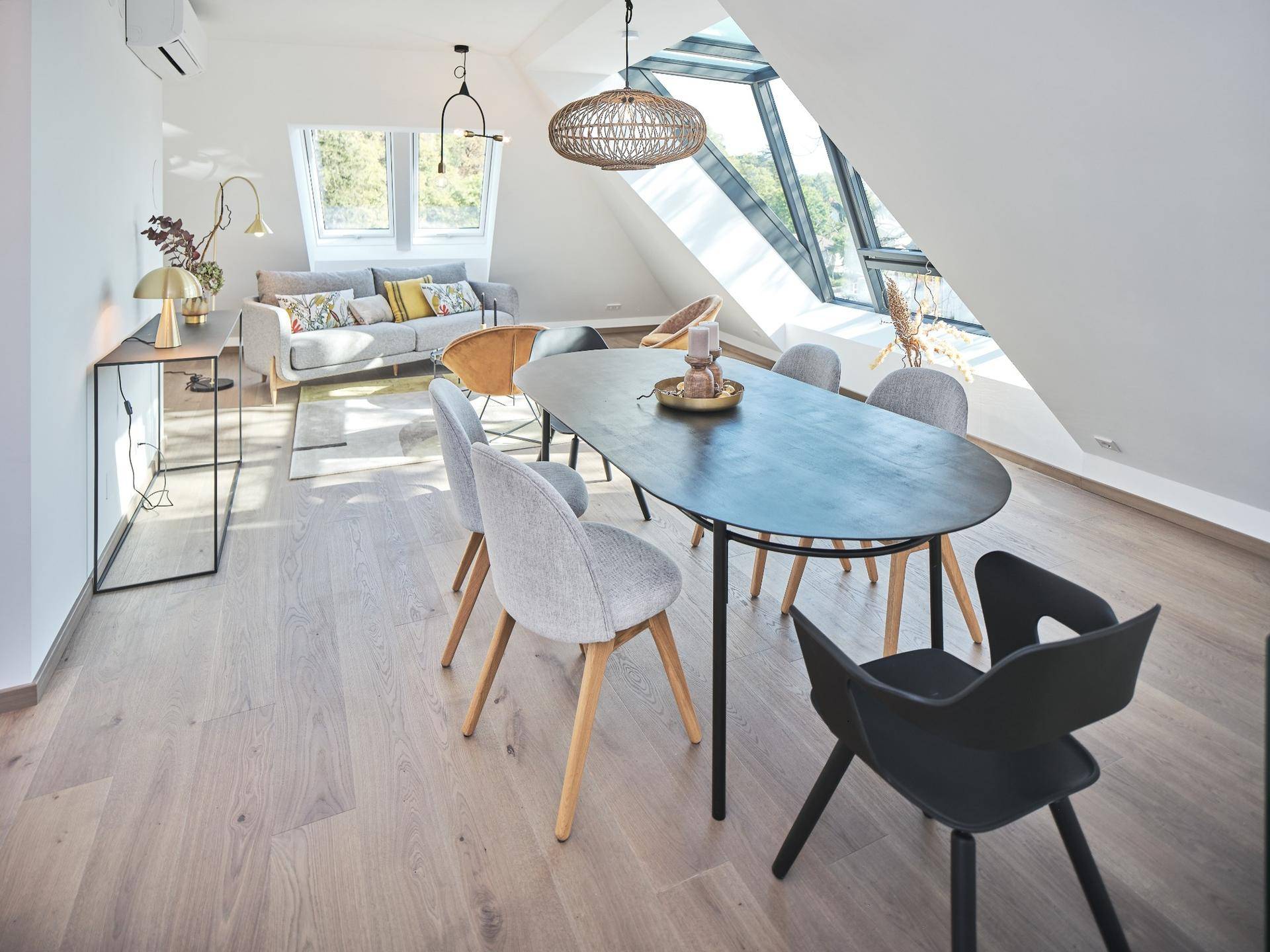 Geräumiger Wohn- und Essbereich mit Holzboden, modernen Möbeln und viel Tageslicht durch Dachfenster.