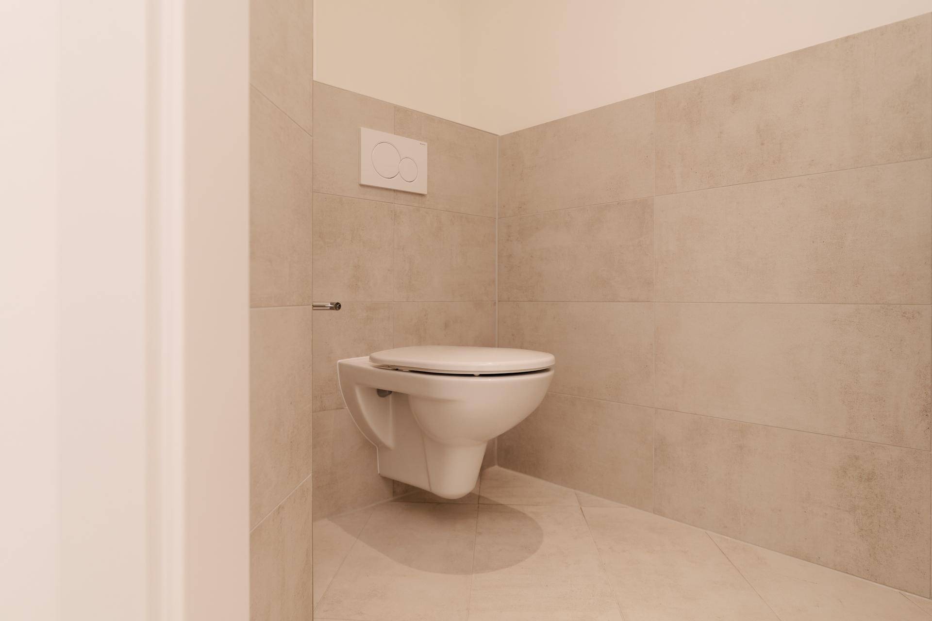 Separates WC mit wandhängender Toilette und modernen Fliesen an Wänden und Boden.