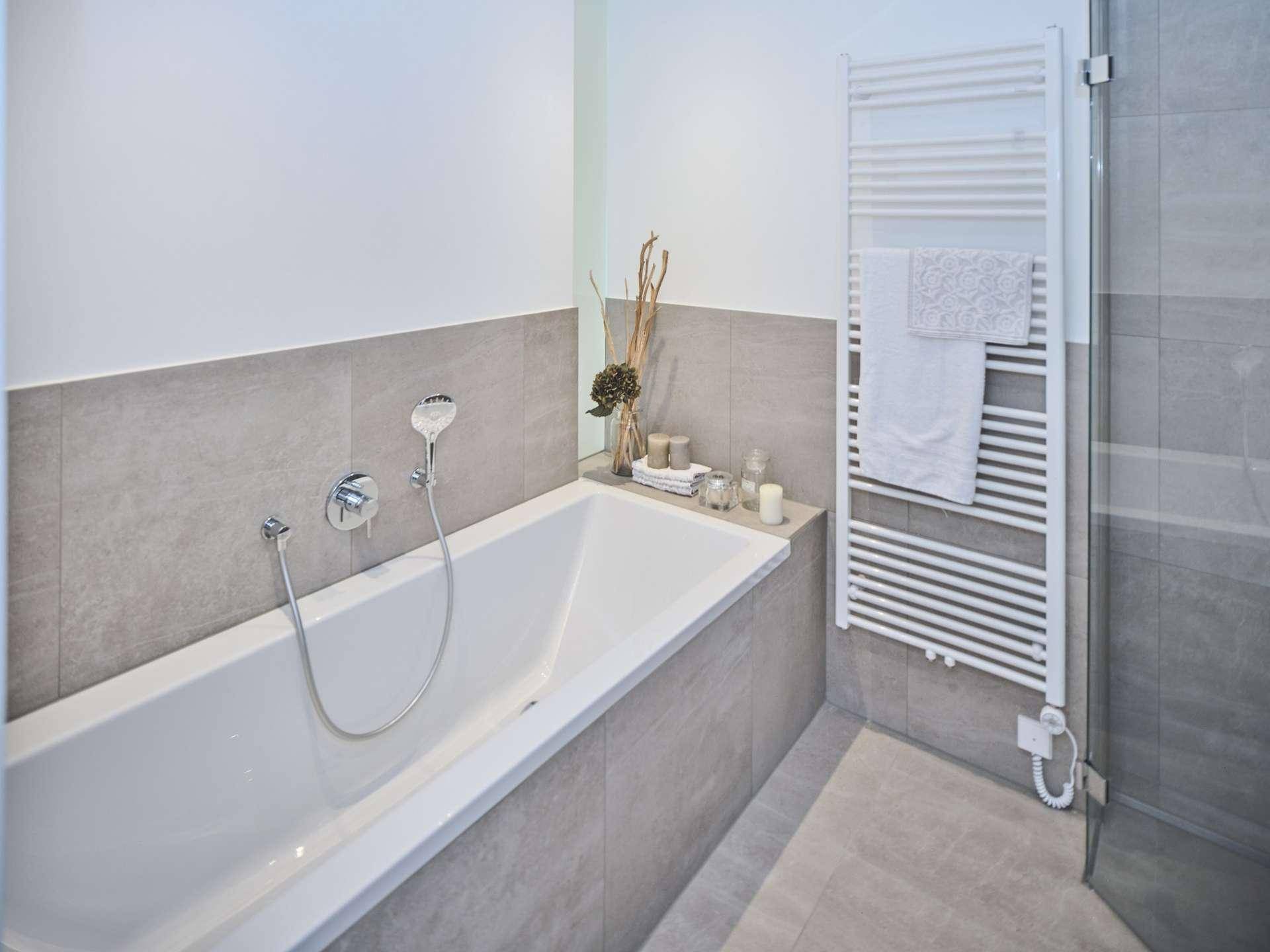 Modernes Badezimmer mit Badewanne, grauen Fliesen und einem praktischen beheizten Handtuchhalter.
