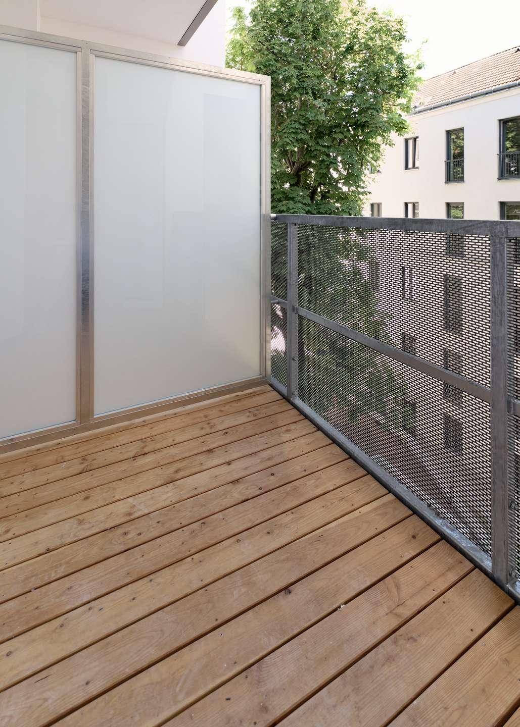 Balkon mit Holzboden und Metallgeländer, bietet einen angenehmen Blick ins Grüne.
