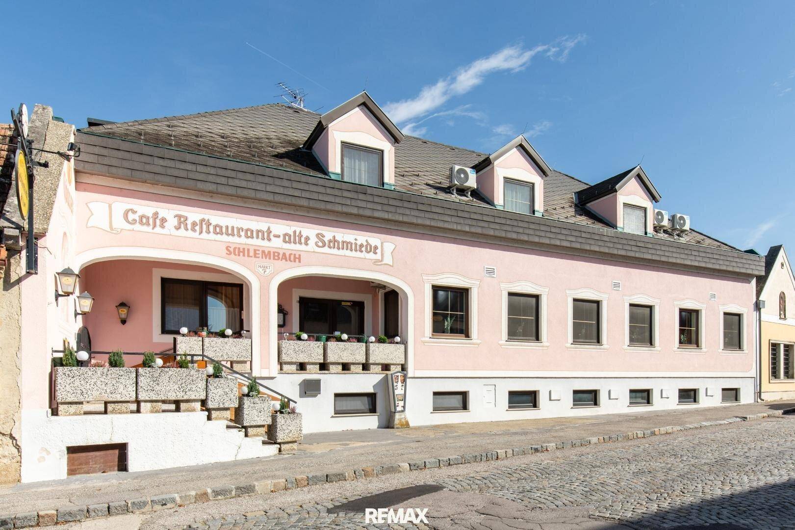 Rosa gestrichenes Gebäude mit der Aufschrift "Cafe Restaurant-alte Schmiede" und einem überdachten Eingangsbereich.