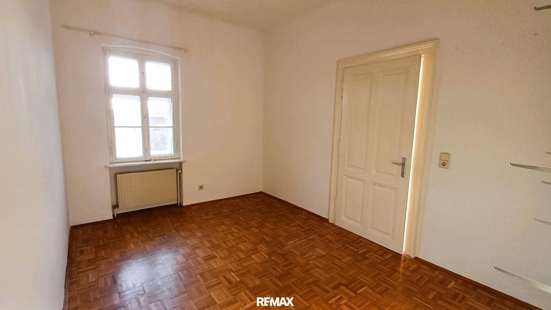 Kleinerer Raum mit Parkettboden, einem Fenster und einer klassischen Holztür.