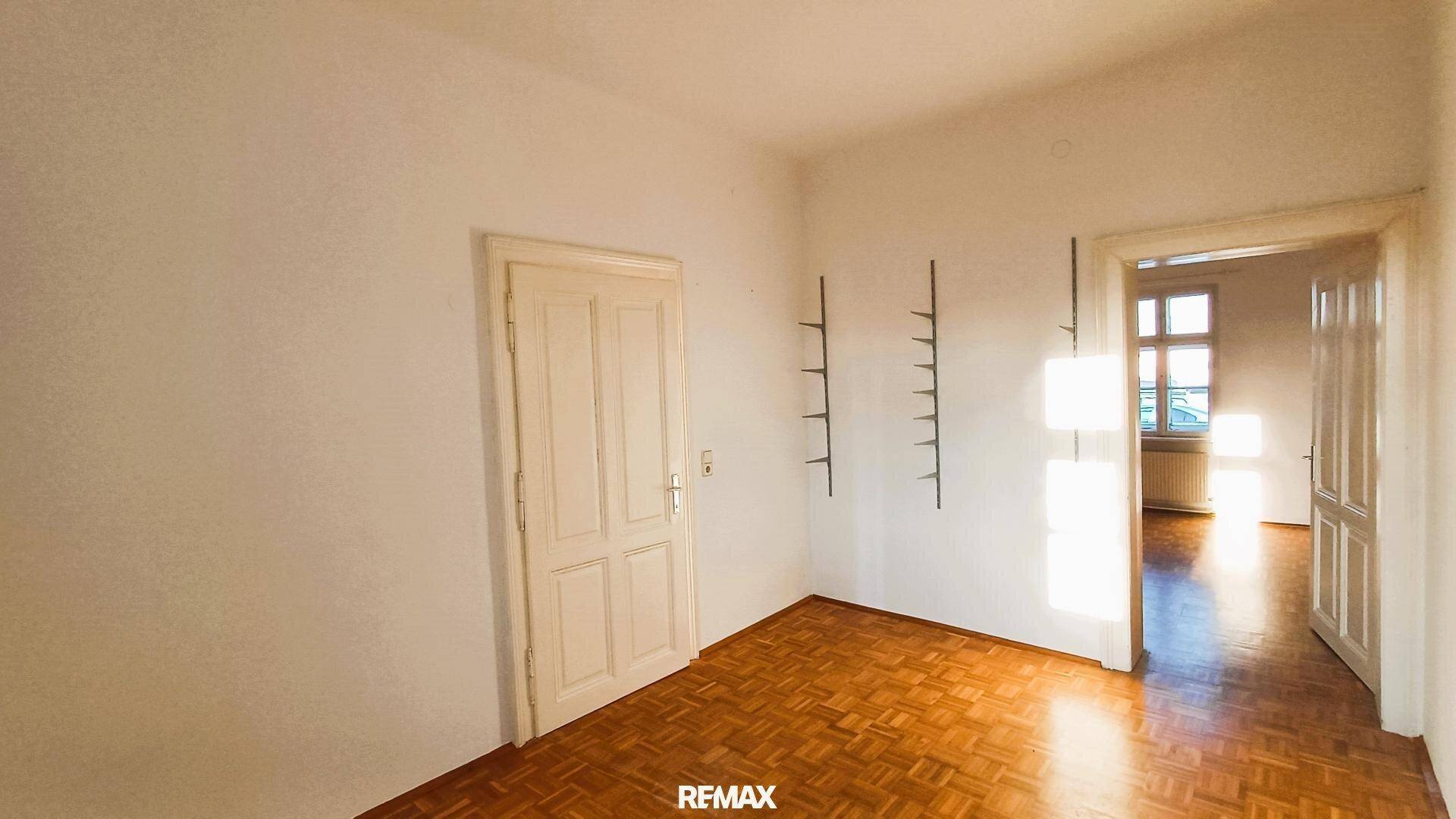 Raum mit Parkettboden und weiß gestrichenen Wänden, mit Blick auf einen weiteren Raum.