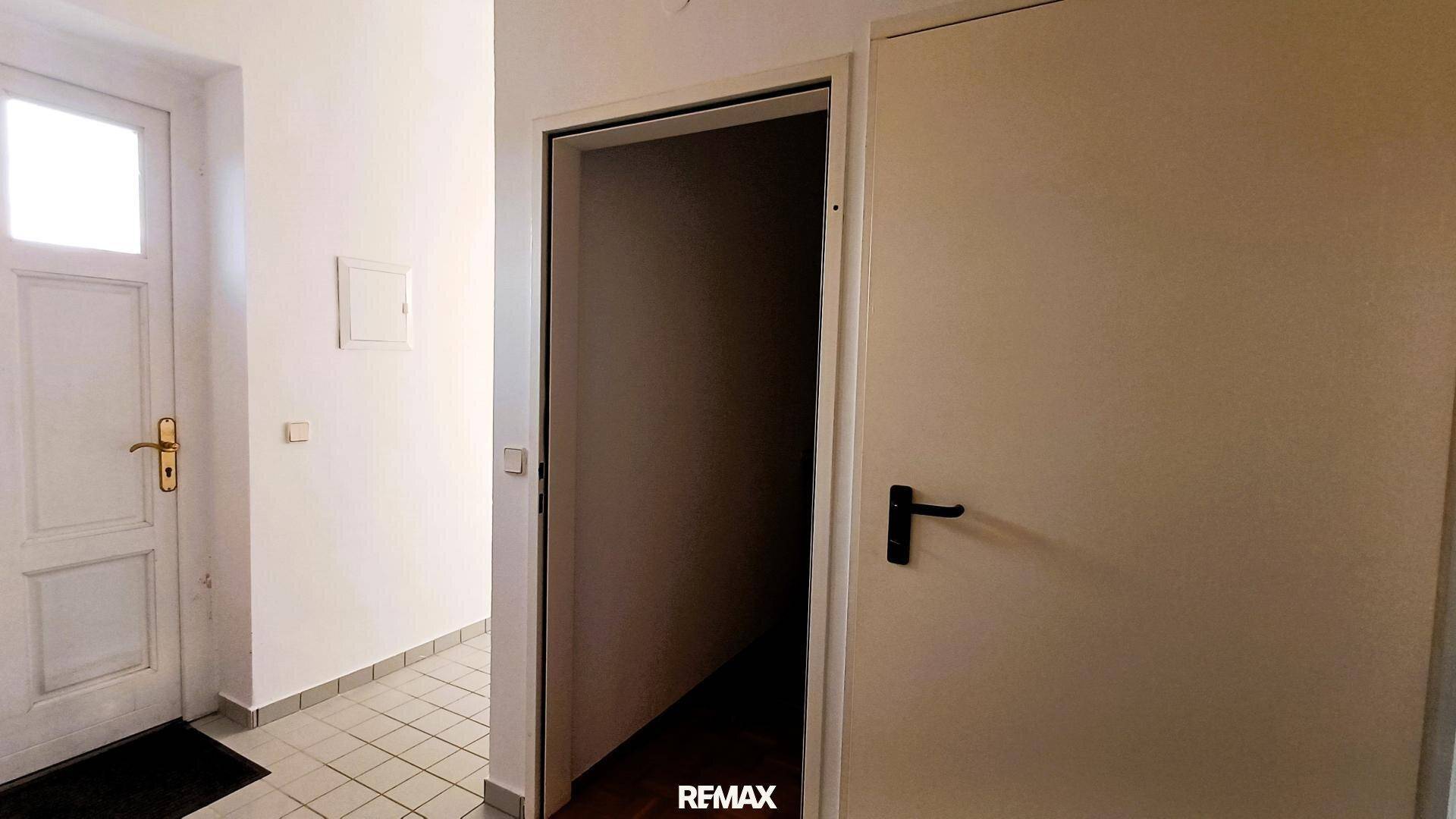 Eingangsbereich mit Fliesenboden und zwei Türen, eine davon führt in einen dunkleren Raum.