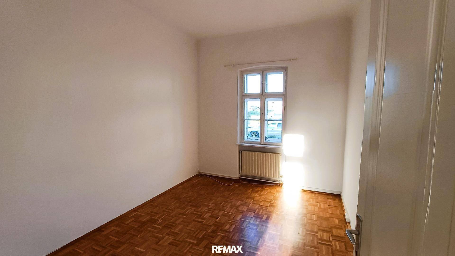 Heller Raum mit Parkettboden, einem Fenster und einem Heizkörper darunter.