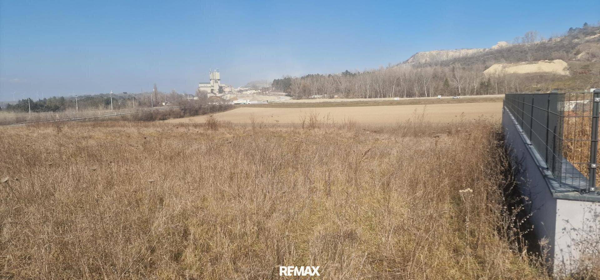 Weitläufige Landschaft mit trockenen Feldern, umgeben von Hügeln und einem Industriegebäude in der Ferne.