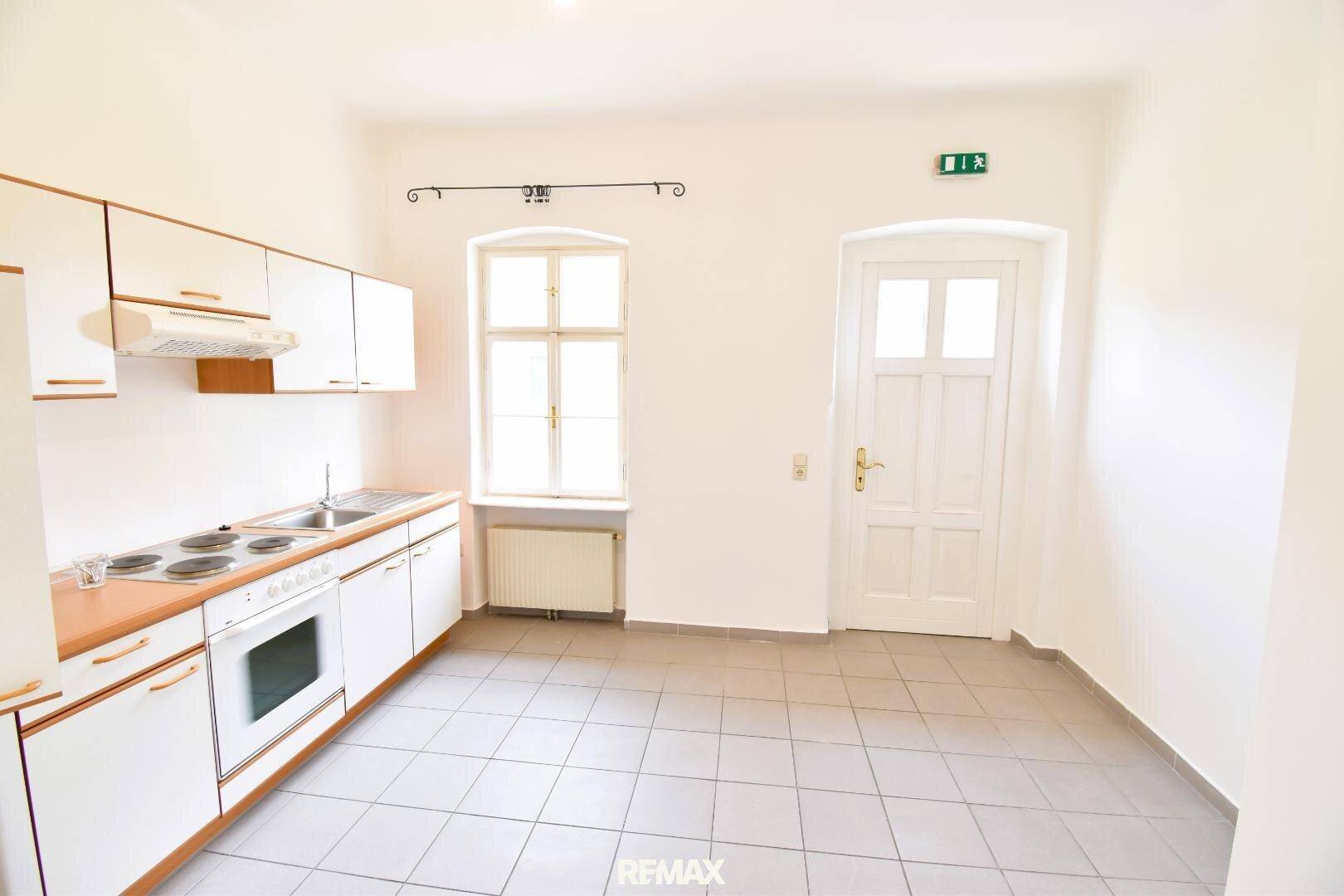 Helle Küche mit weißen Schränken, hellbraunen Arbeitsplatten, gefliestem Boden und einem Fenster.