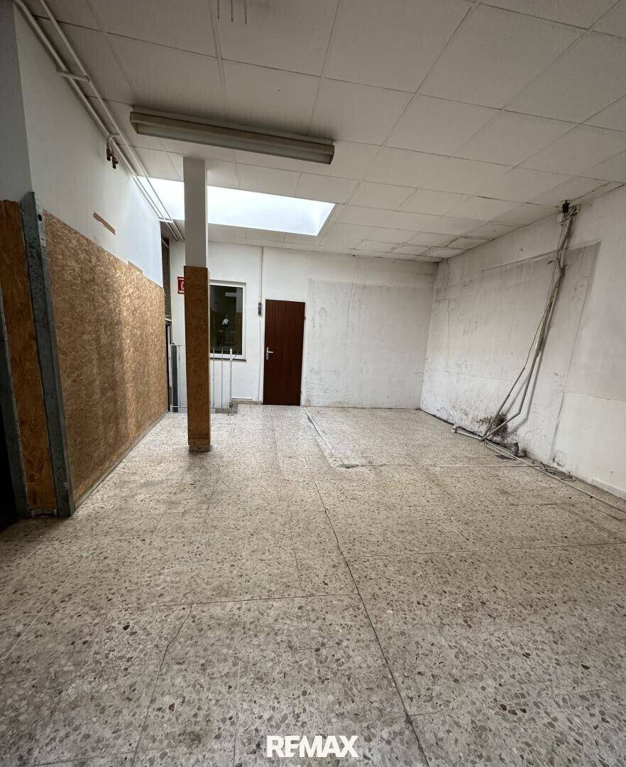 Innenansicht eines Gewerberaums mit Terrazzoboden, einer Holztür und einem Oberlicht in der Decke.