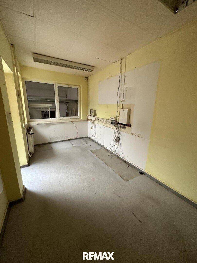 Kleinerer Raum mit gelben Wänden, einem Fenster und sichtbaren Kabelinstallationen an der Wand.