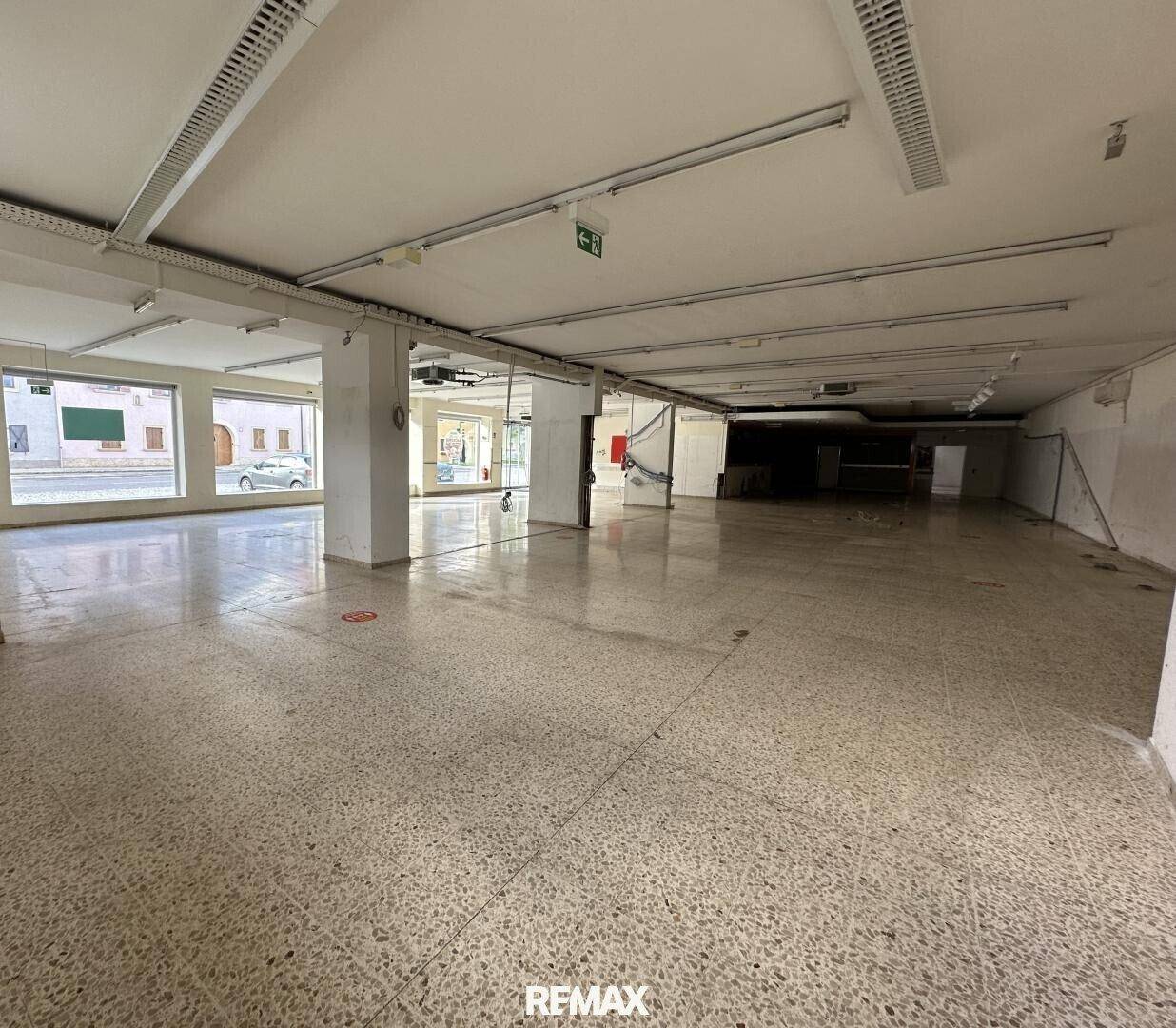 Großer, offener Gewerberaum mit Terrazzoboden und Blick auf die Straße durch die breiten Fenster.