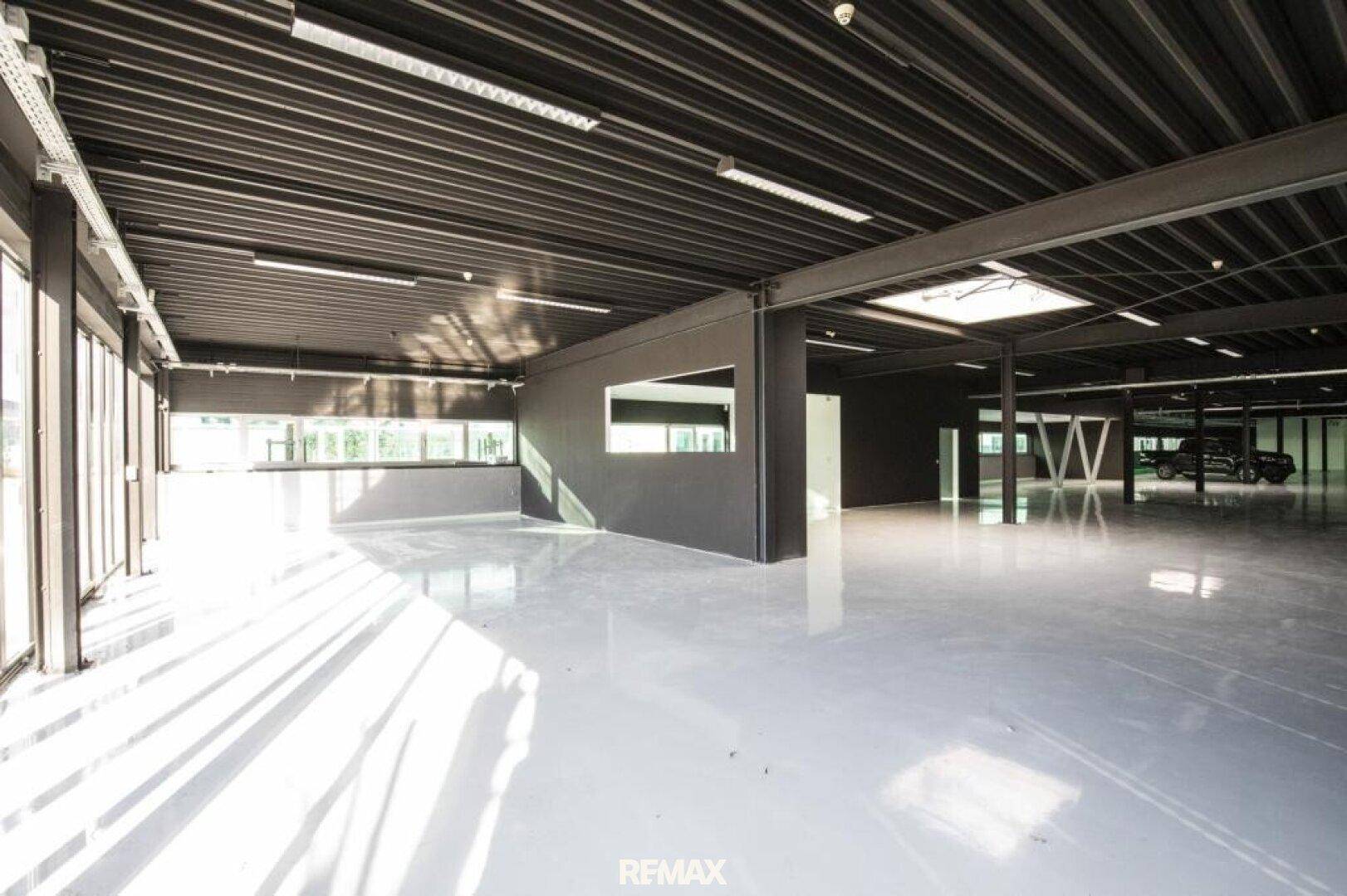 Weitläufige Gewerbefläche mit dunkler Decke und großen Fenstern, die viel Tageslicht hereinlassen.