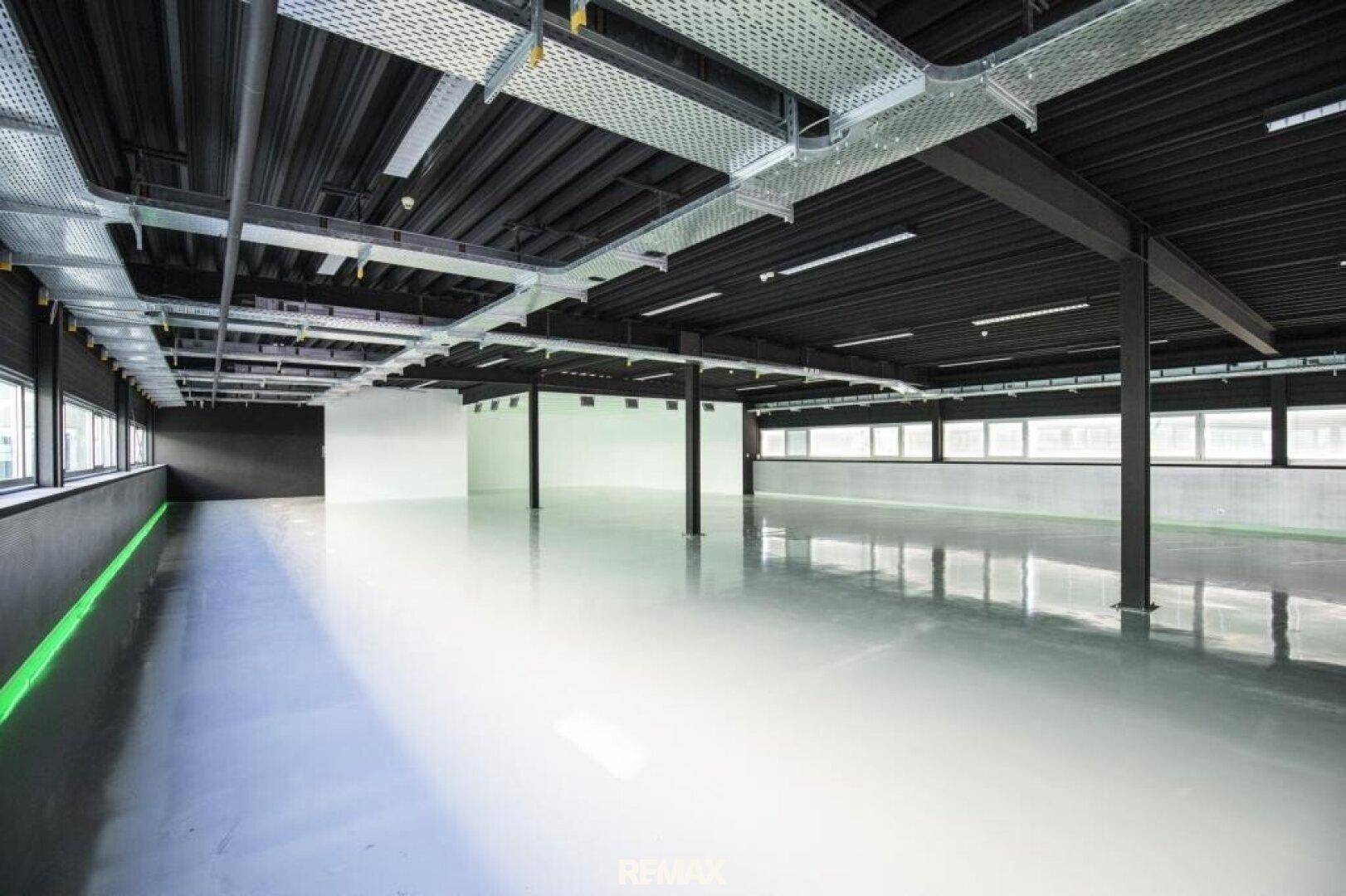 Große, offene Gewerbefläche mit sichtbaren Installationen an der Decke und viel Tageslicht.