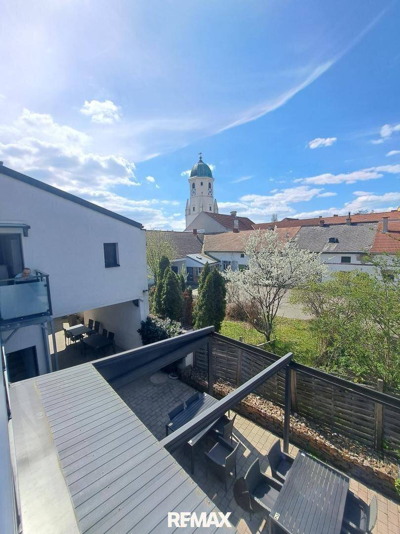 Weitläufiger Blick über eine Terrasse mit Sitzgelegenheiten und Kirchturm im Hintergrund.