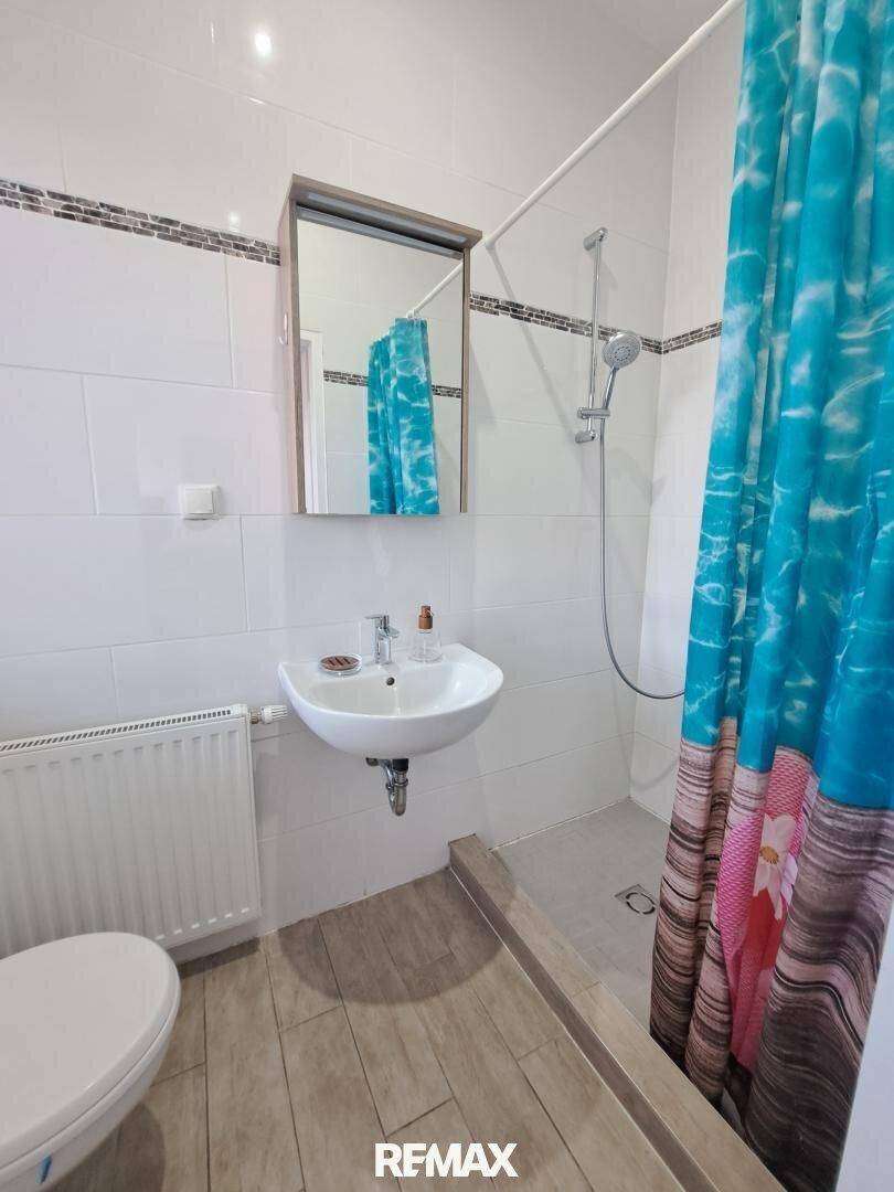 Modernes Badezimmer mit Dusche, WC, Waschbecken und Heizkörper.